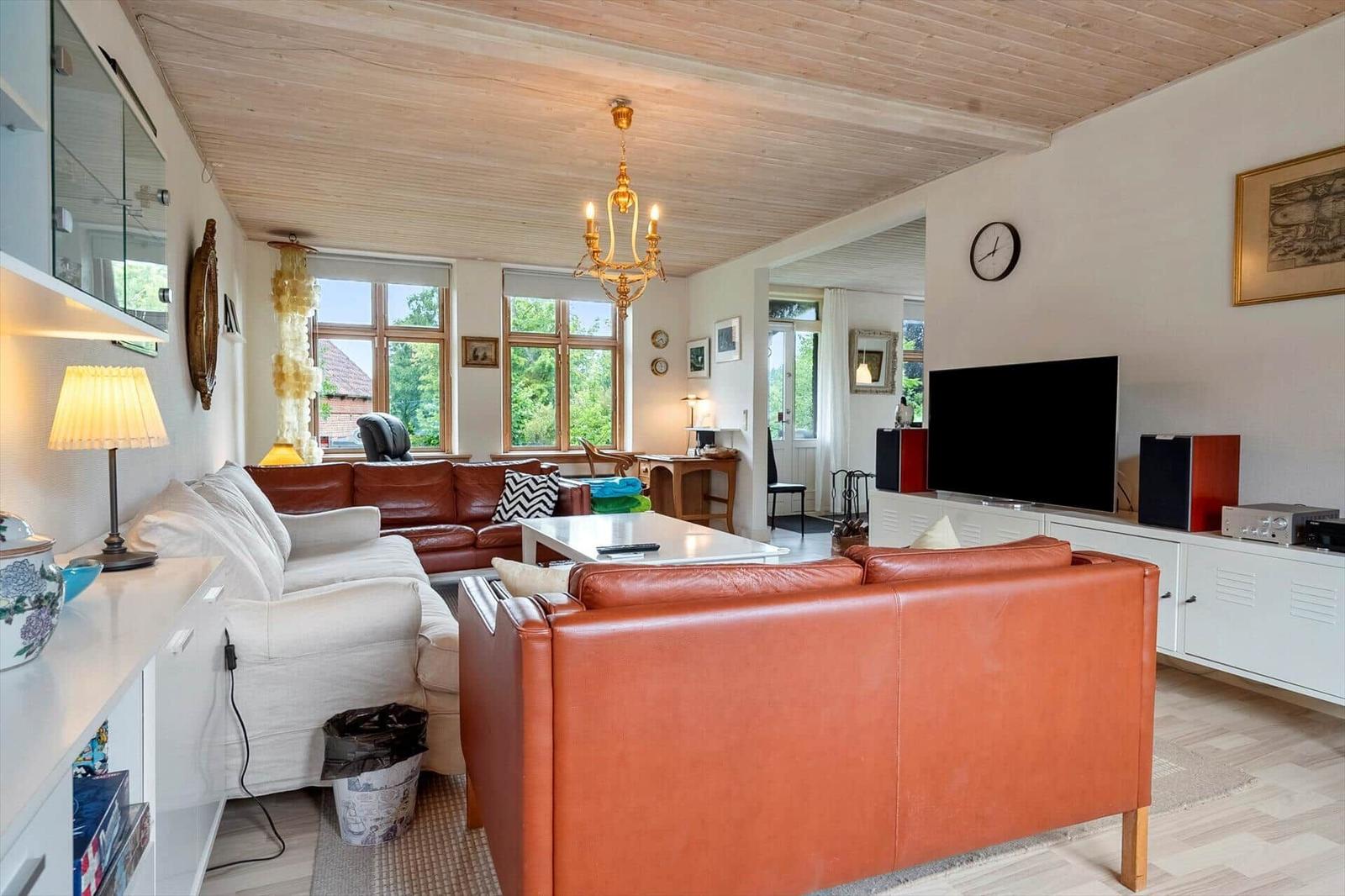 Wohnzimmer mit braunem Ledersofa, weißen Sofas und Holzdecke.