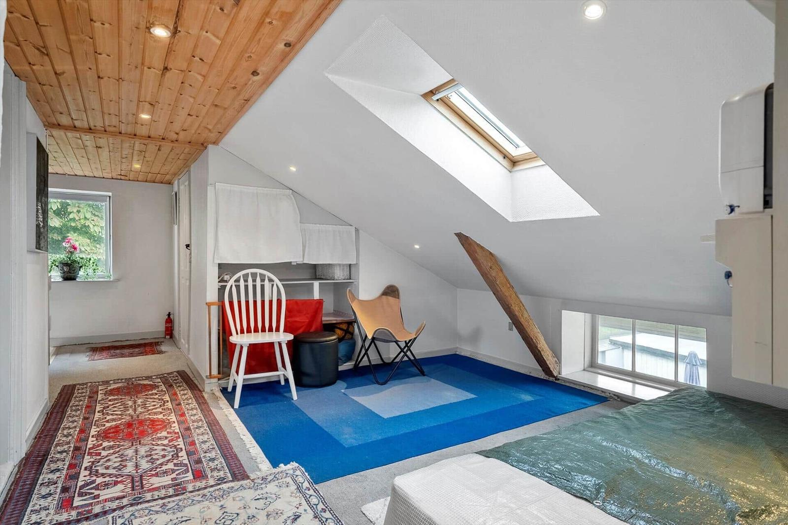 Dachgeschosszimmer mit Holzdecke, Dachfenster, blauem Boden und weißen Wänden.