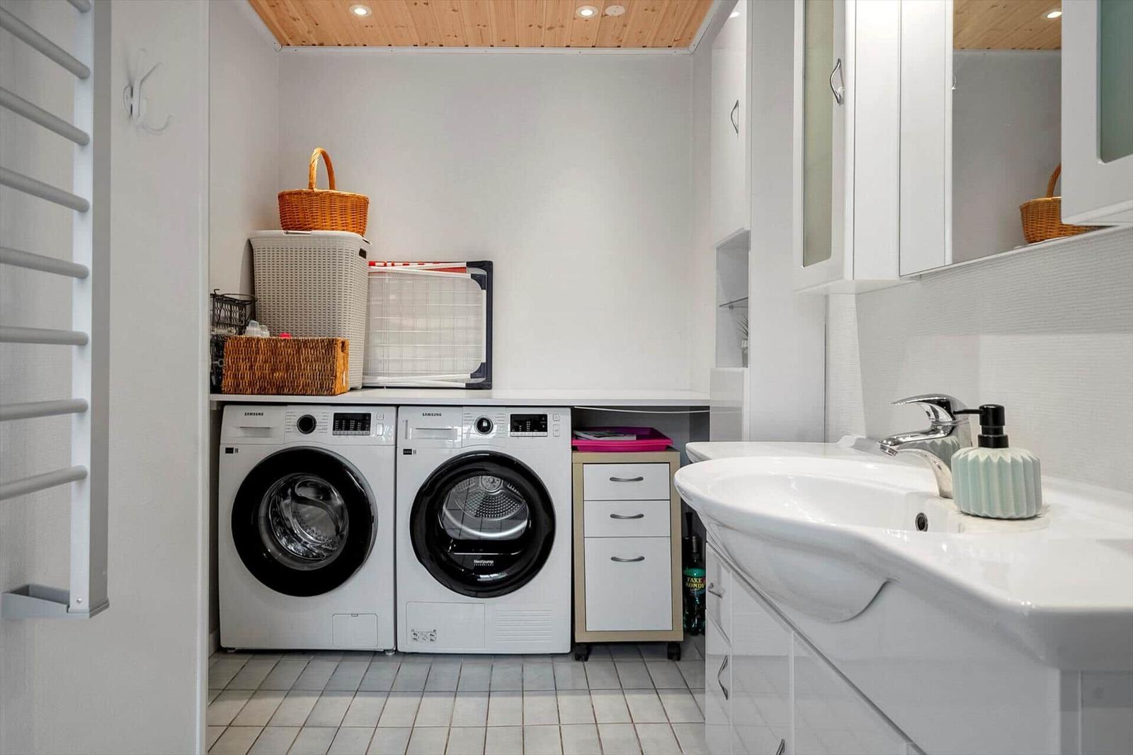 Waschmaschine und Trockner stehen neben Waschbecken mit Spiegel.