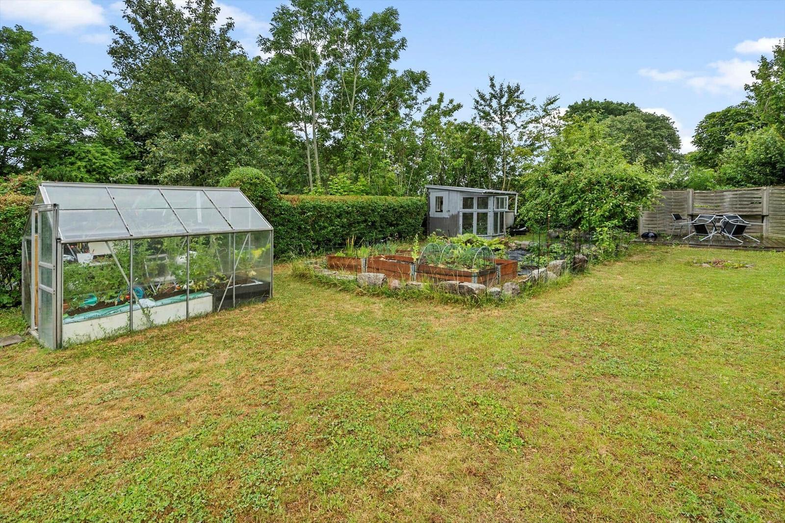Hinterhof mit Gemüsegarten, Gewächshaus und Sitzgelegenheit.