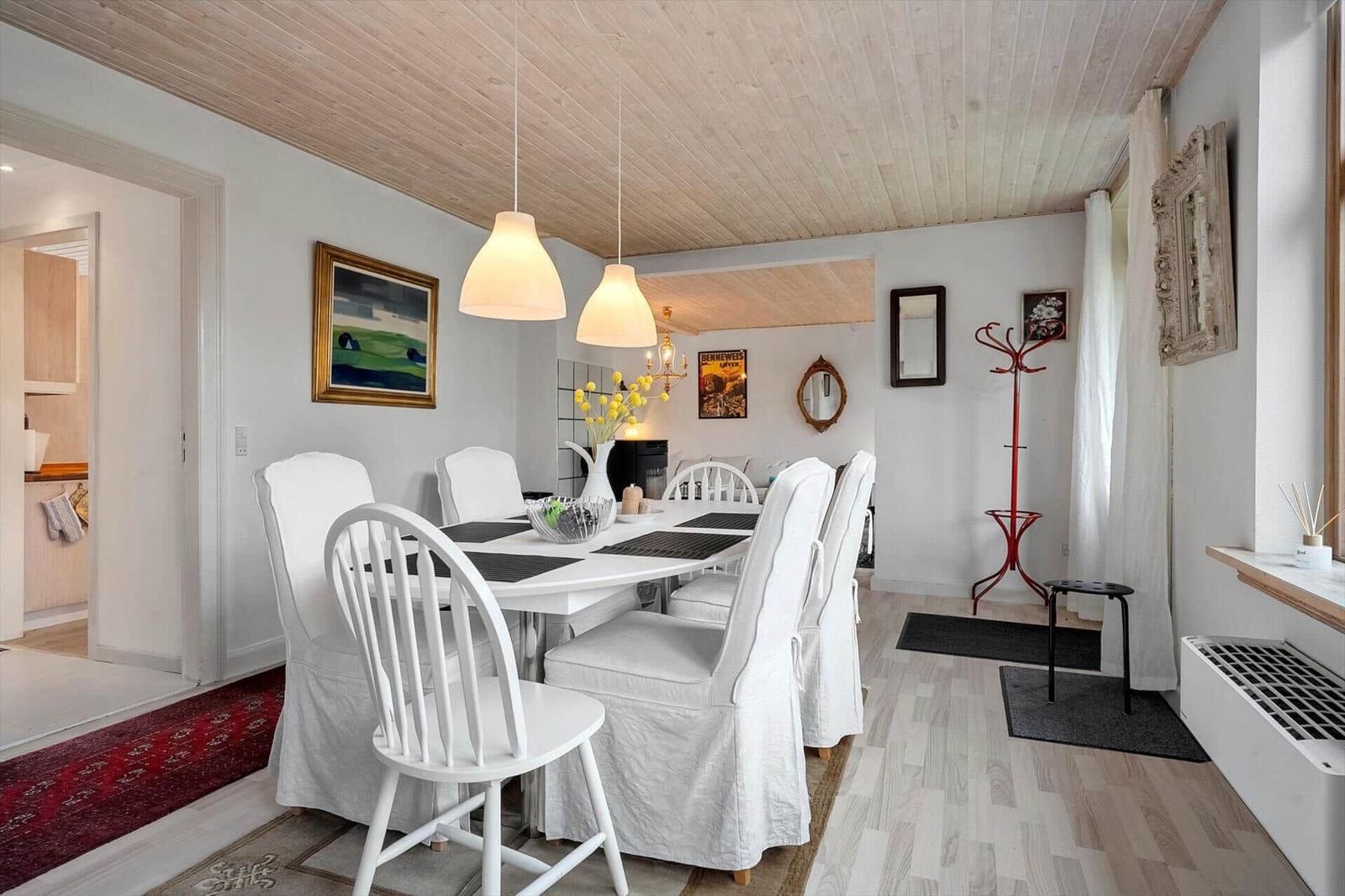 Essbereich mit weißem Tisch und Stühlen, Holzdecke und Wanddekoration.