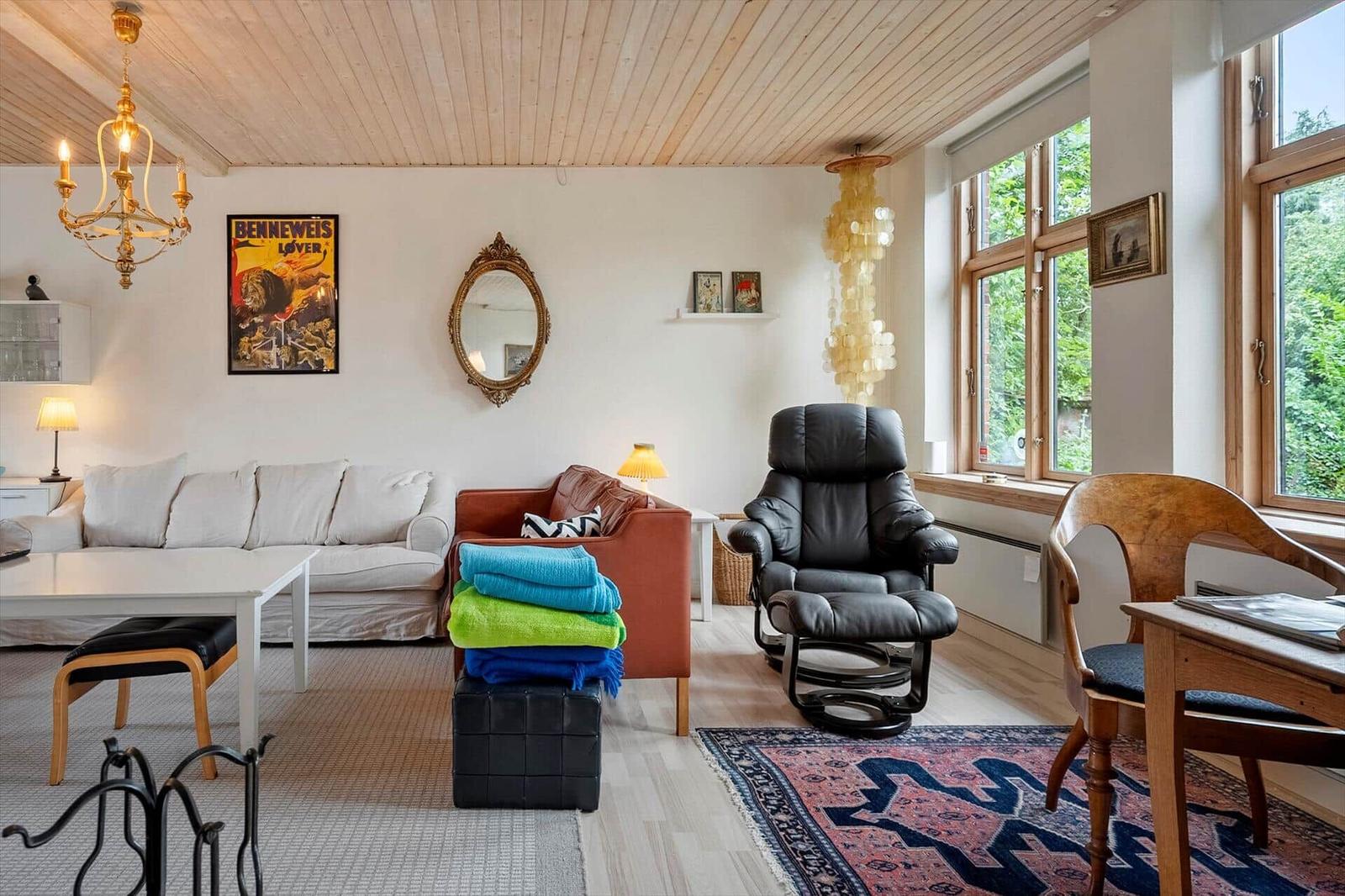 Wohnzimmer mit Sofa, Sessel und Fenster mit Blick auf Grün.