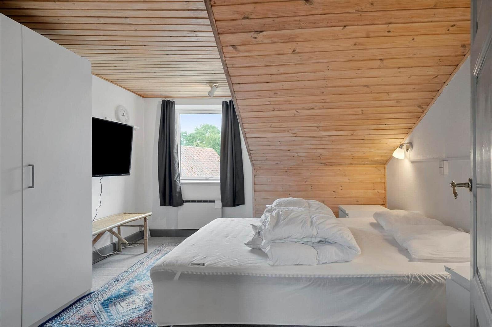 Schlafzimmer mit Doppelbett, Holzdecke, TV und Fenster mit Blick.