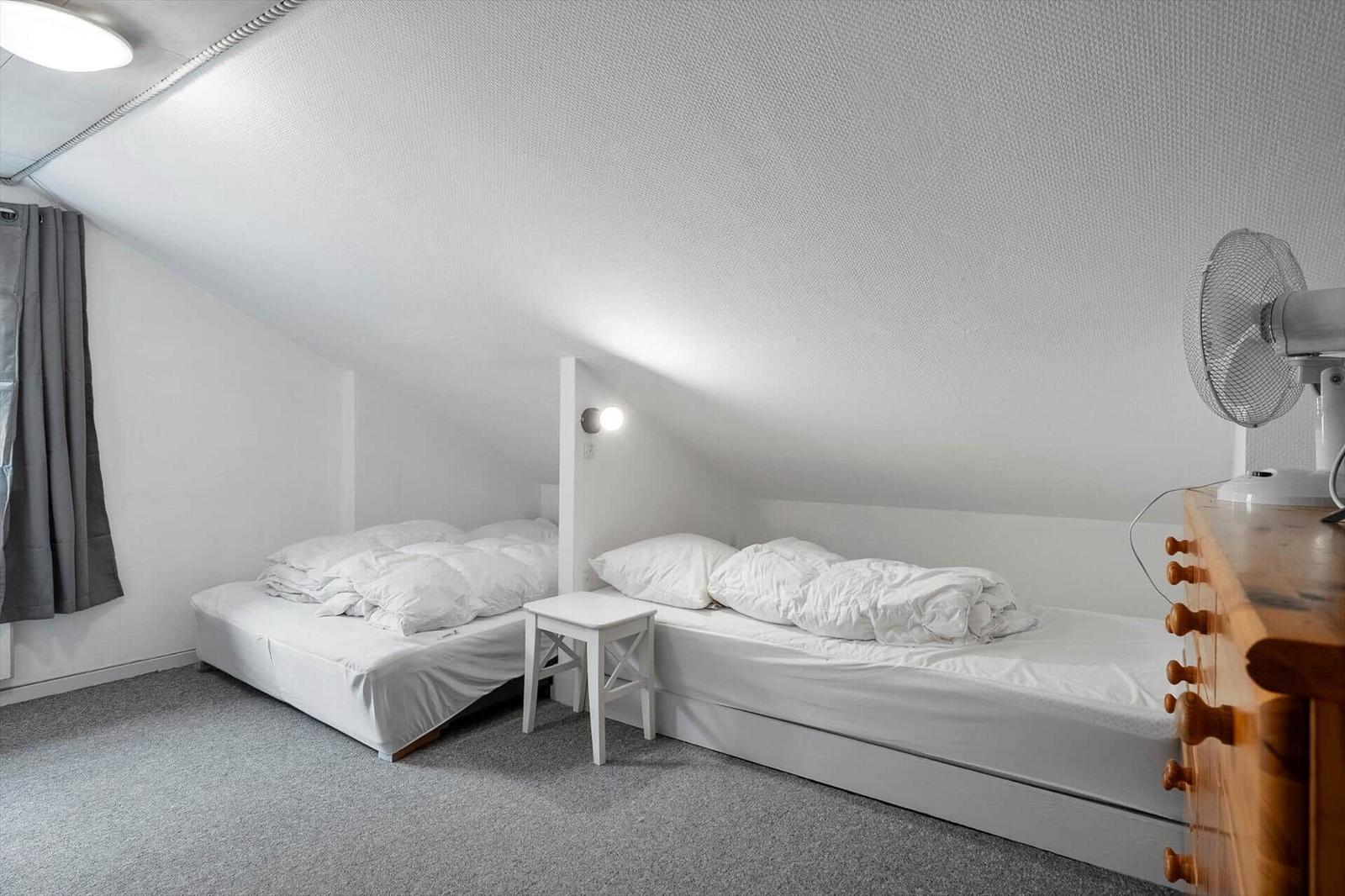 Zwei Betten in einem Dachzimmer mit Holzkommode und Ventilator.