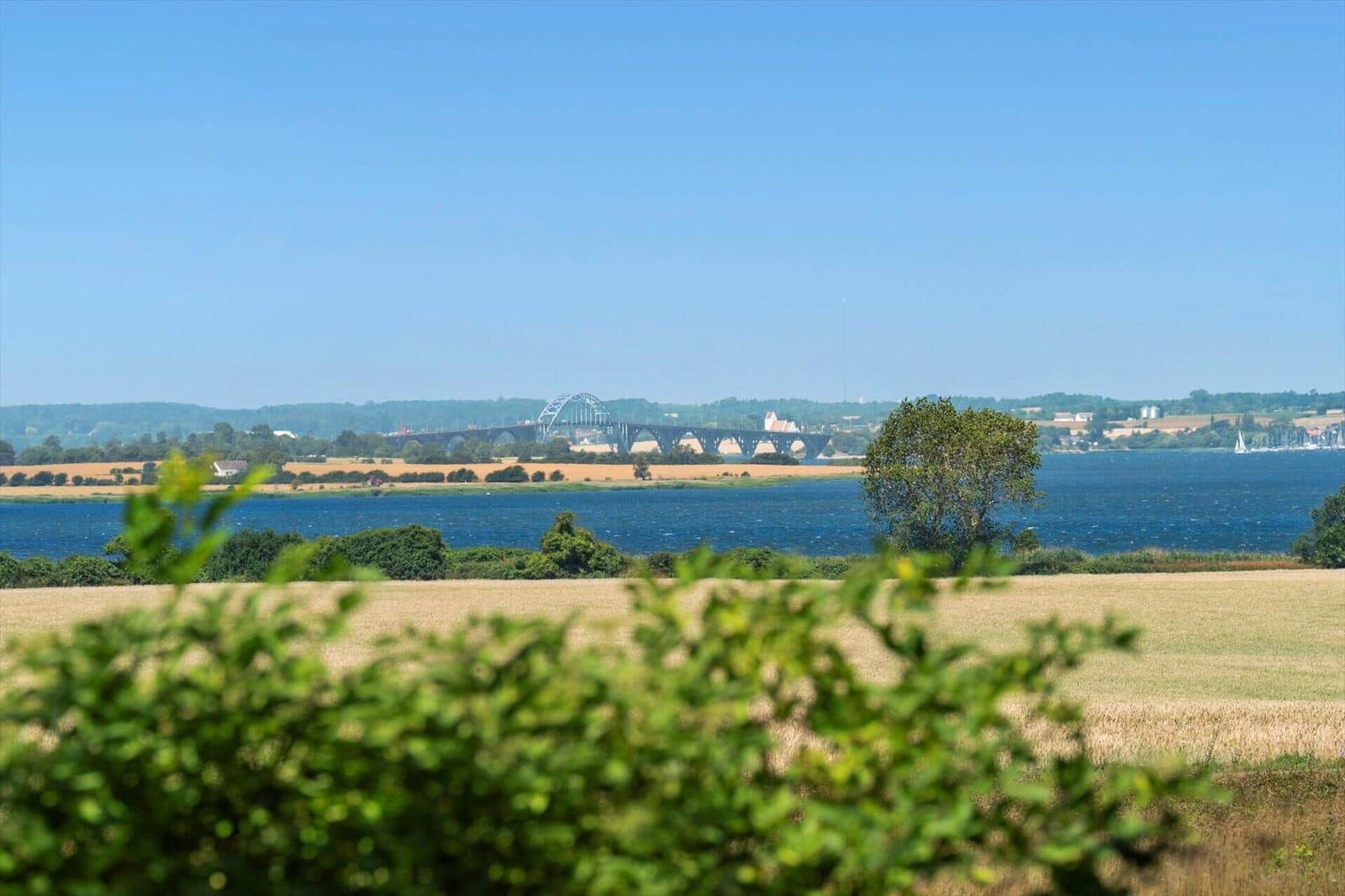 Wide view of river, bridge, and fields under blue sky.