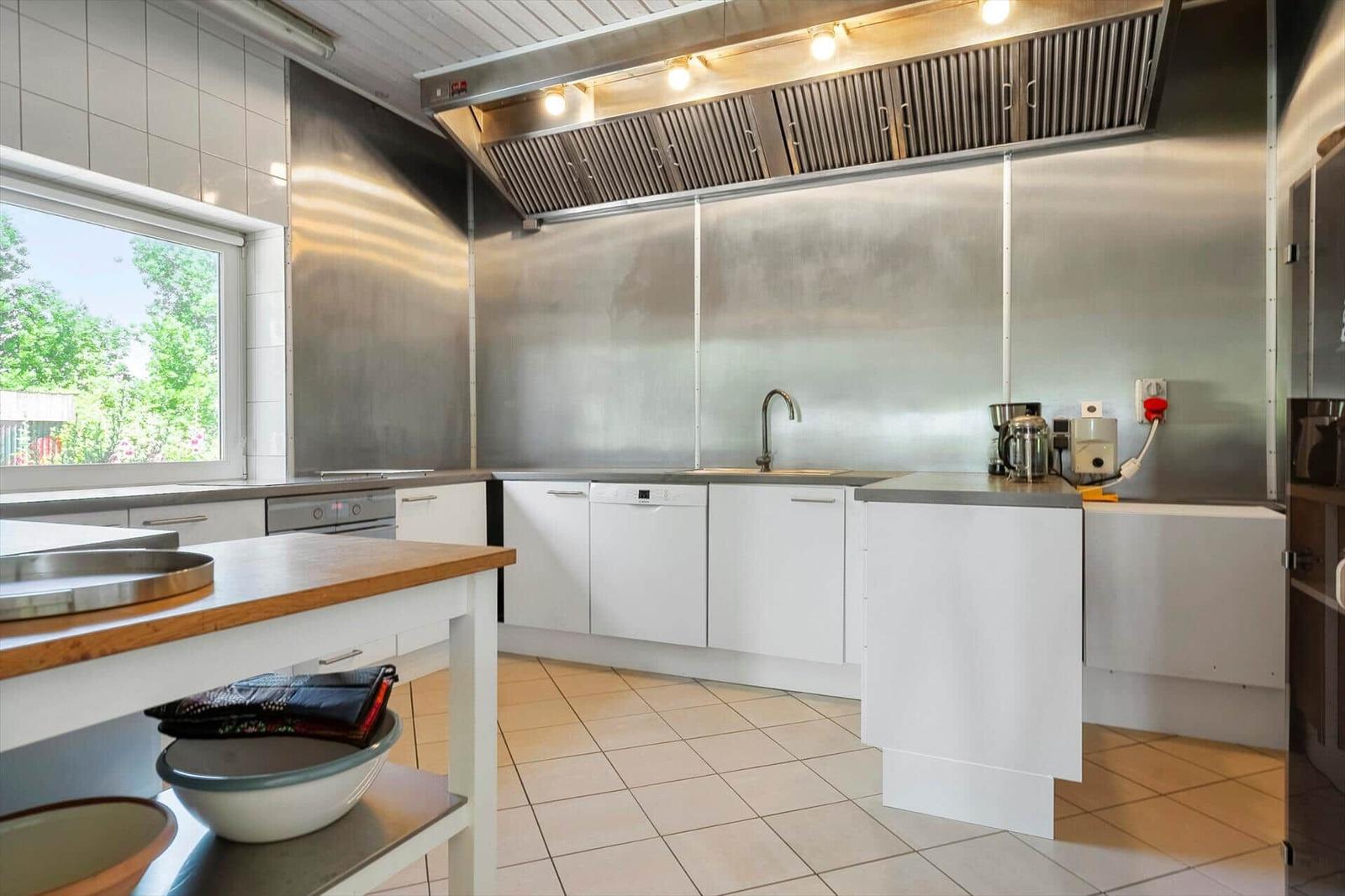 Modern kitchen with stainless steel wall, countertops, and garden view through window.