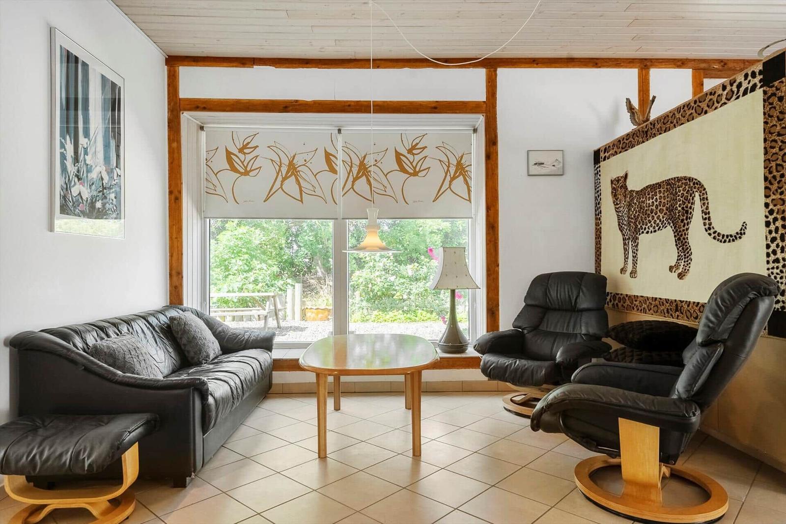 Living room with leather sofa, two chairs, and large window overlooking garden.