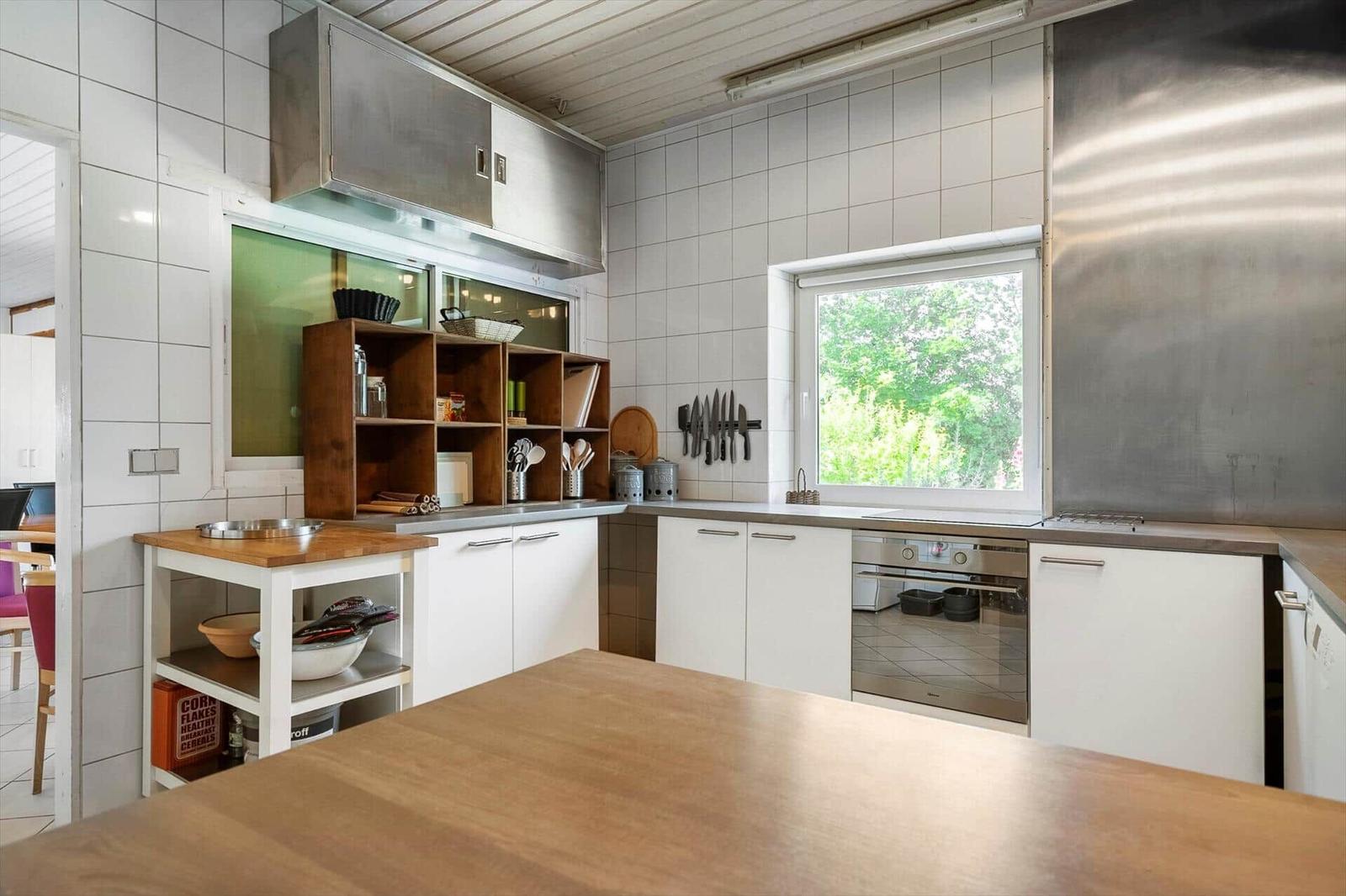 Kitchen with white cabinets, stainless steel hood, and wooden table. Window shows green trees.