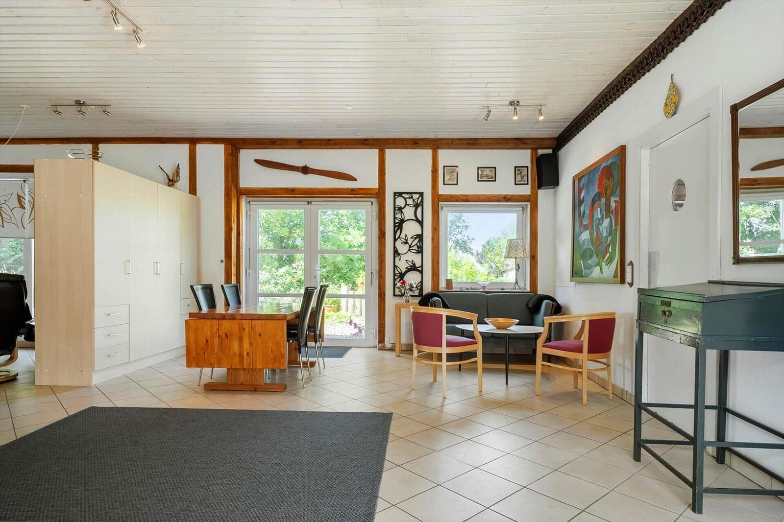 Large living and dining area with wooden ceiling, windows, and modern furniture.