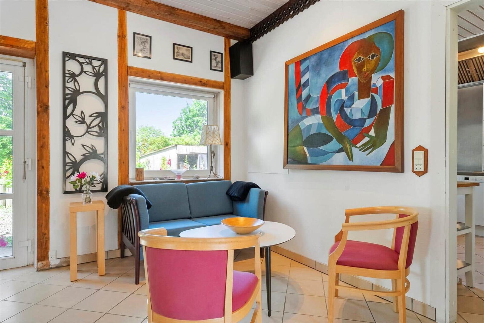 Living area with sofa, two chairs, and wall art. View of garden through window.