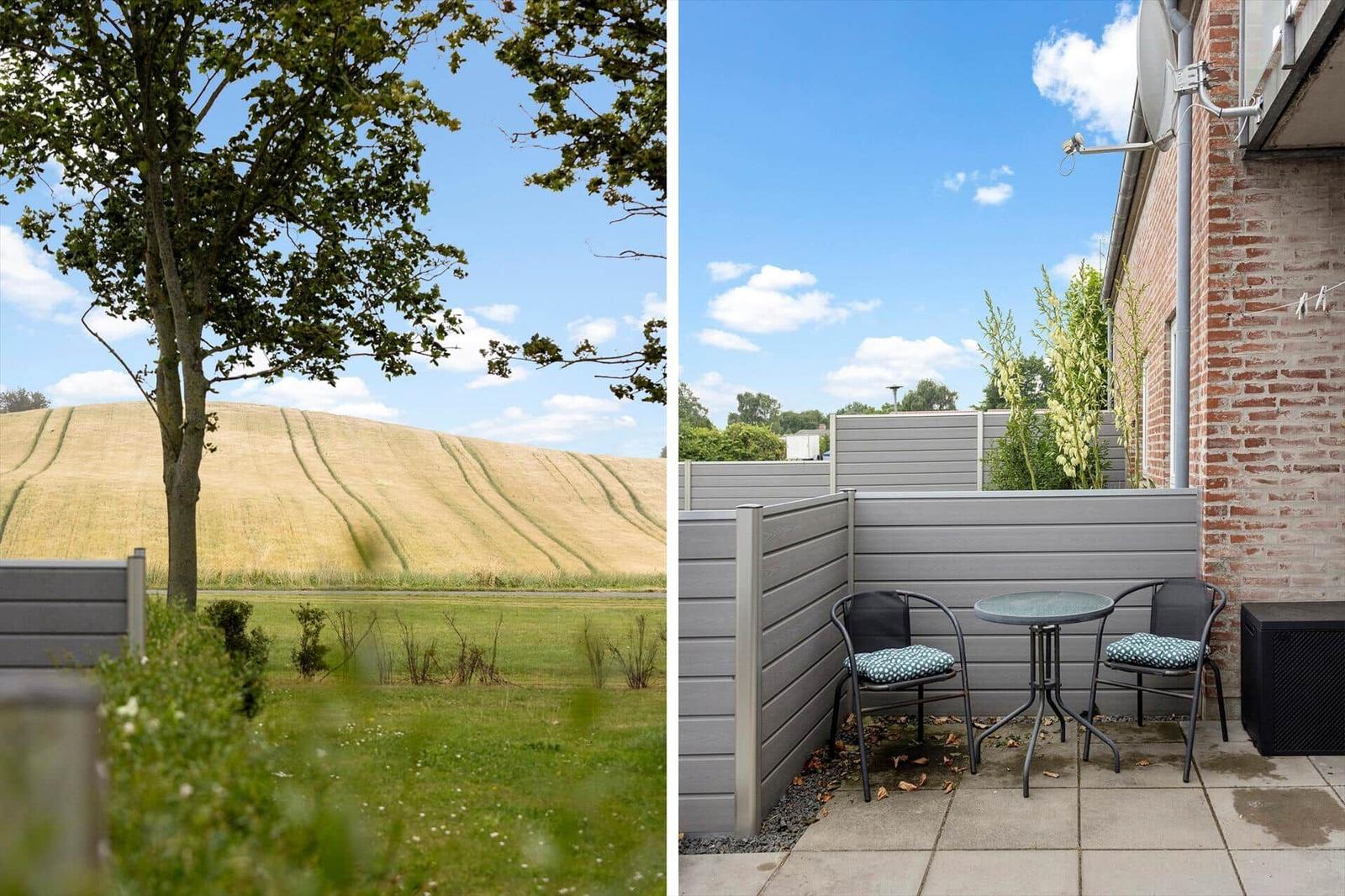 Terrasse mit Tisch und zwei Stühlen neben Backsteinhaus. Blick auf Feld und Baum.