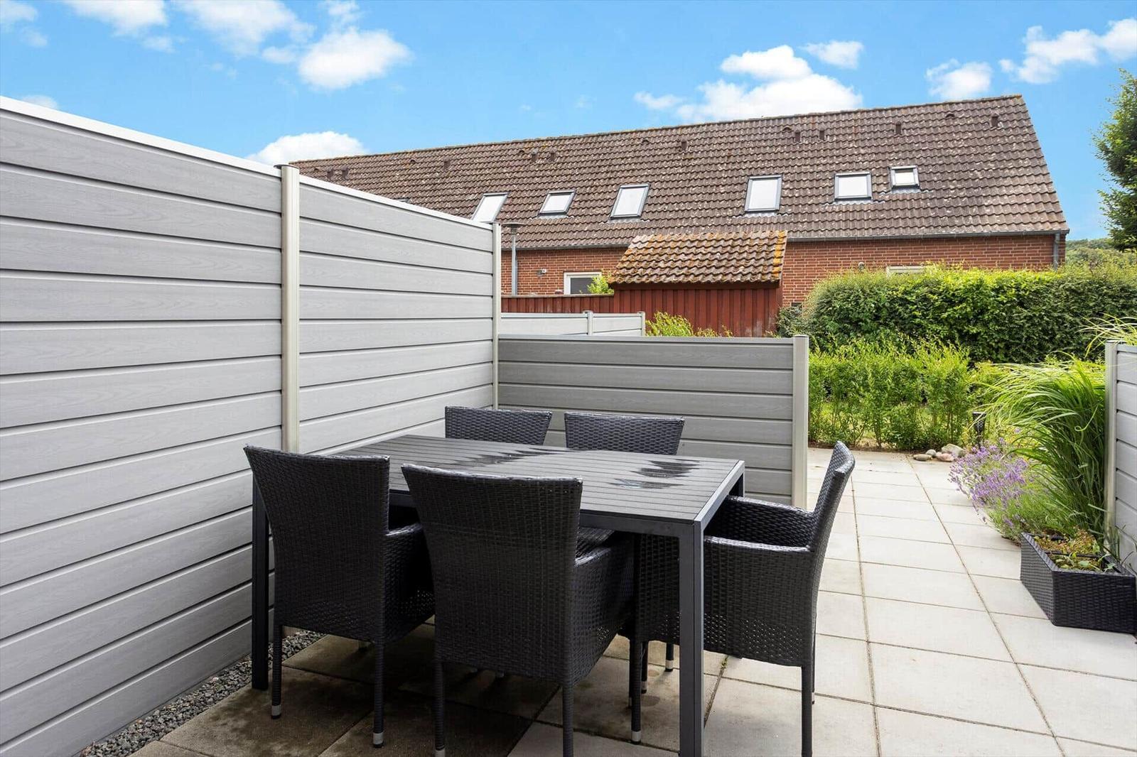 Terrasse mit Tisch und Stühlen, umgeben von grauen Sichtschutzwänden und grüner Vegetation.