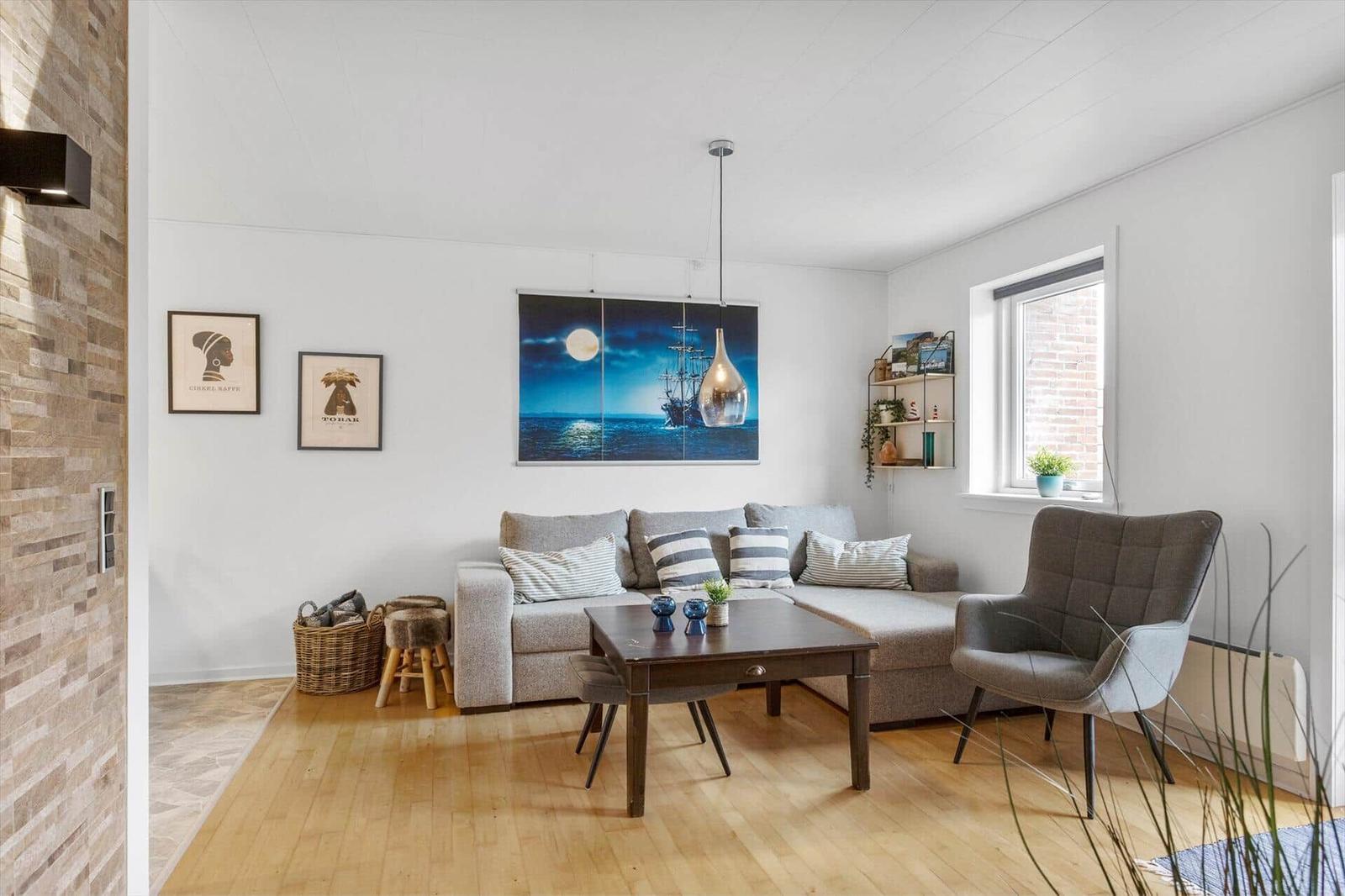 Wohnzimmer mit Sofa, Sitzgelegenheit und Wandbild. Holzboden und Fenster.