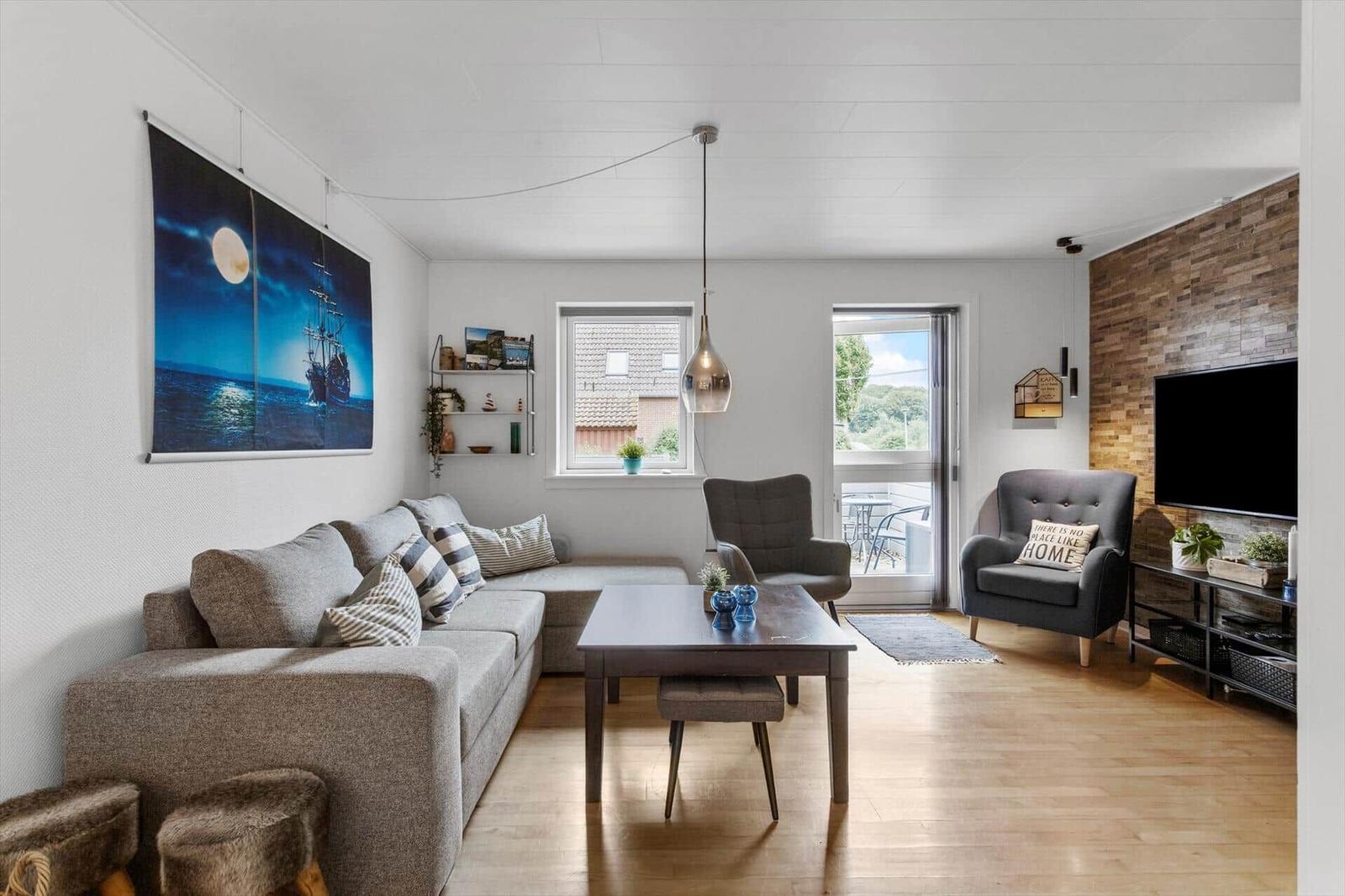 Wohnzimmer mit Sofa, Tisch und Fernseher an Holzwand. Tür führt auf Balkon.