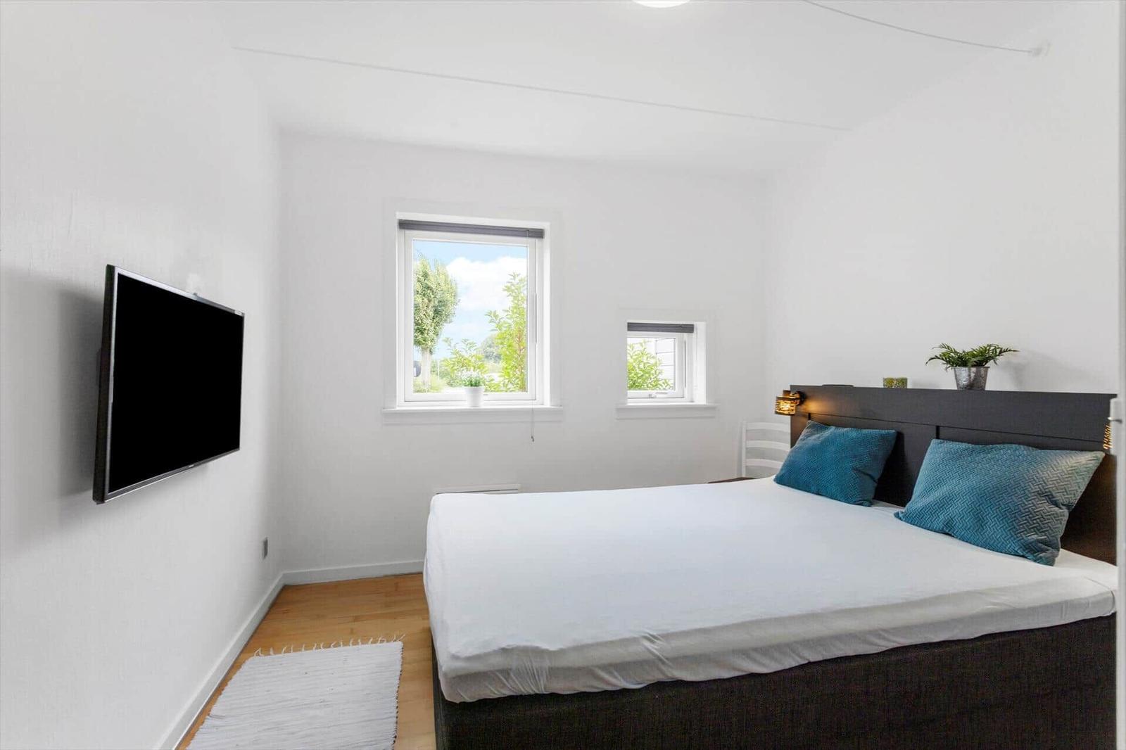 Schlafzimmer mit Bett, Fernseher und Fenstern.