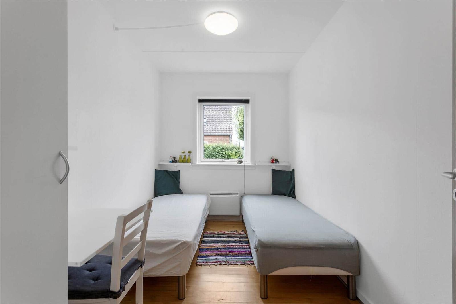 Zwei Einzelbetten stehen im Raum. Fenster, Teppich und Stuhl sind sichtbar.