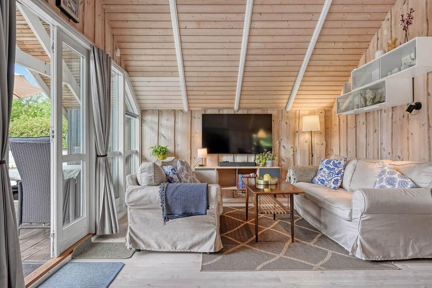 Wohnzimmer mit Sofa, Sessel, Fernseher und Terrassentür.