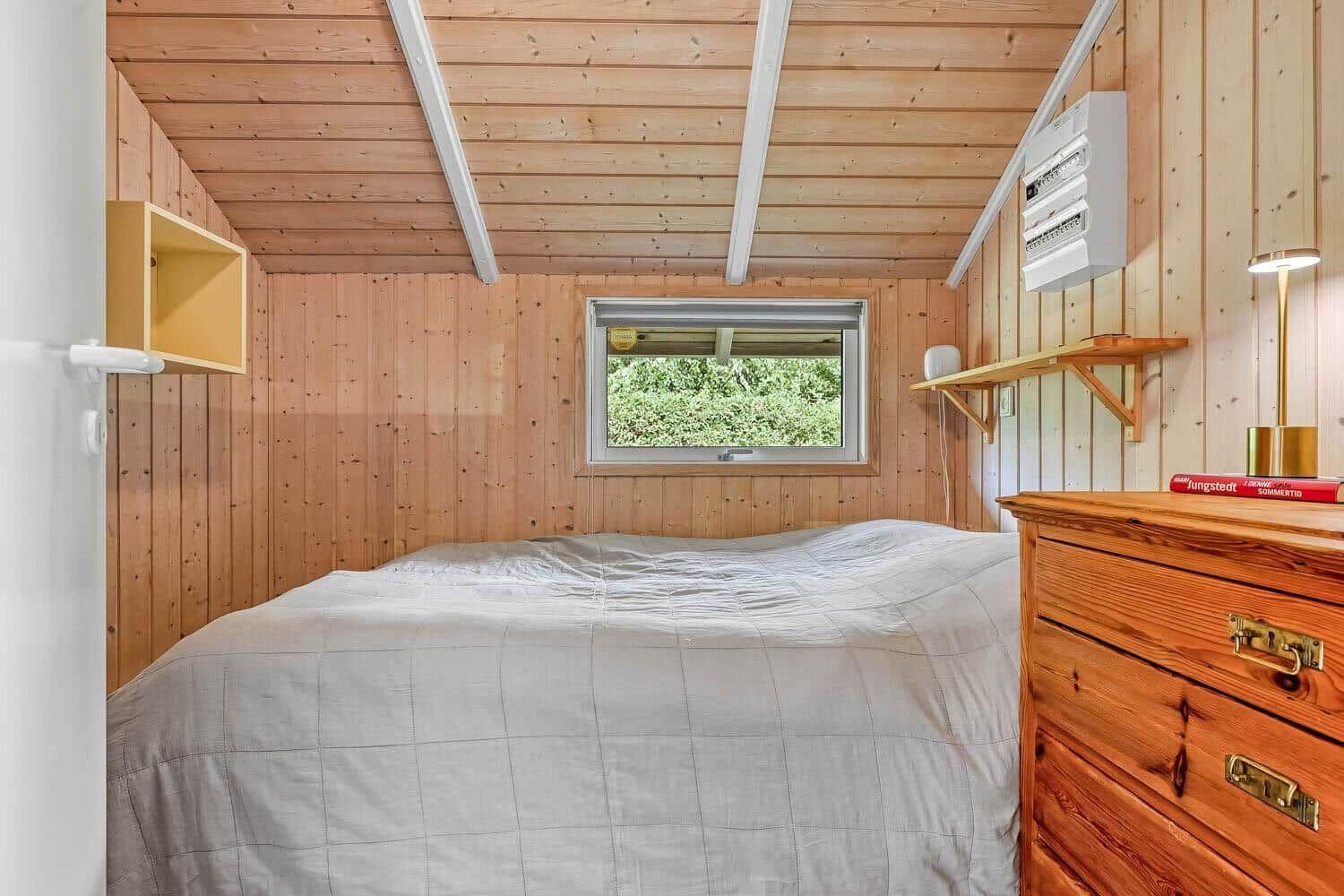 Schlafzimmer mit Holzwand, Bett und Fenster mit Blick auf Grün.