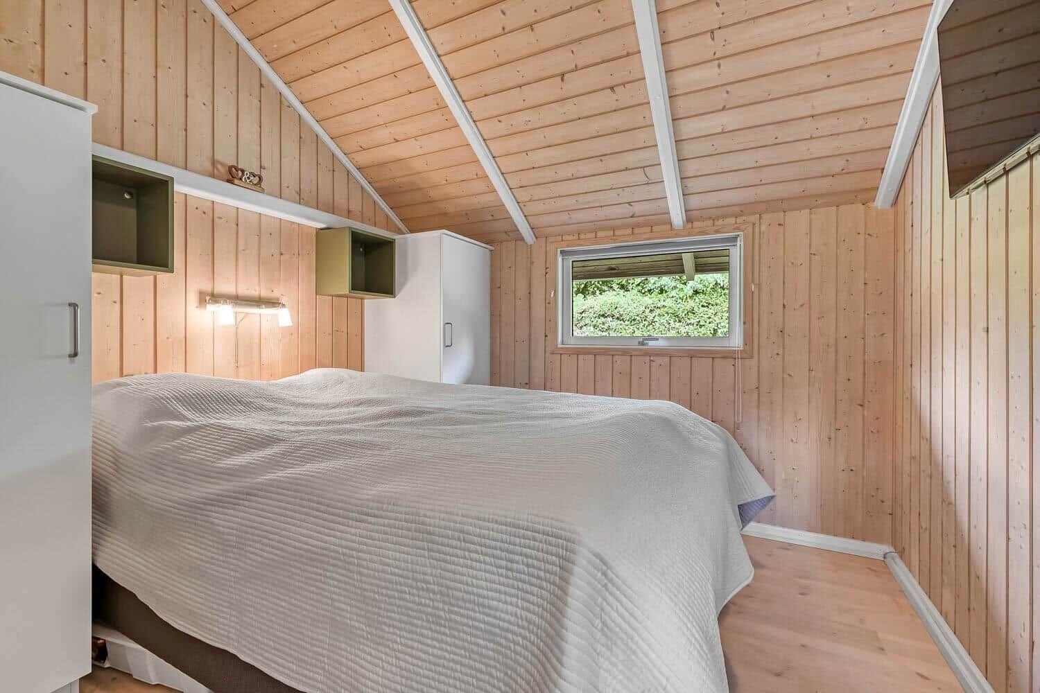 Schlafzimmer mit Holzwand, Bett und Fenster zur Außenseite.