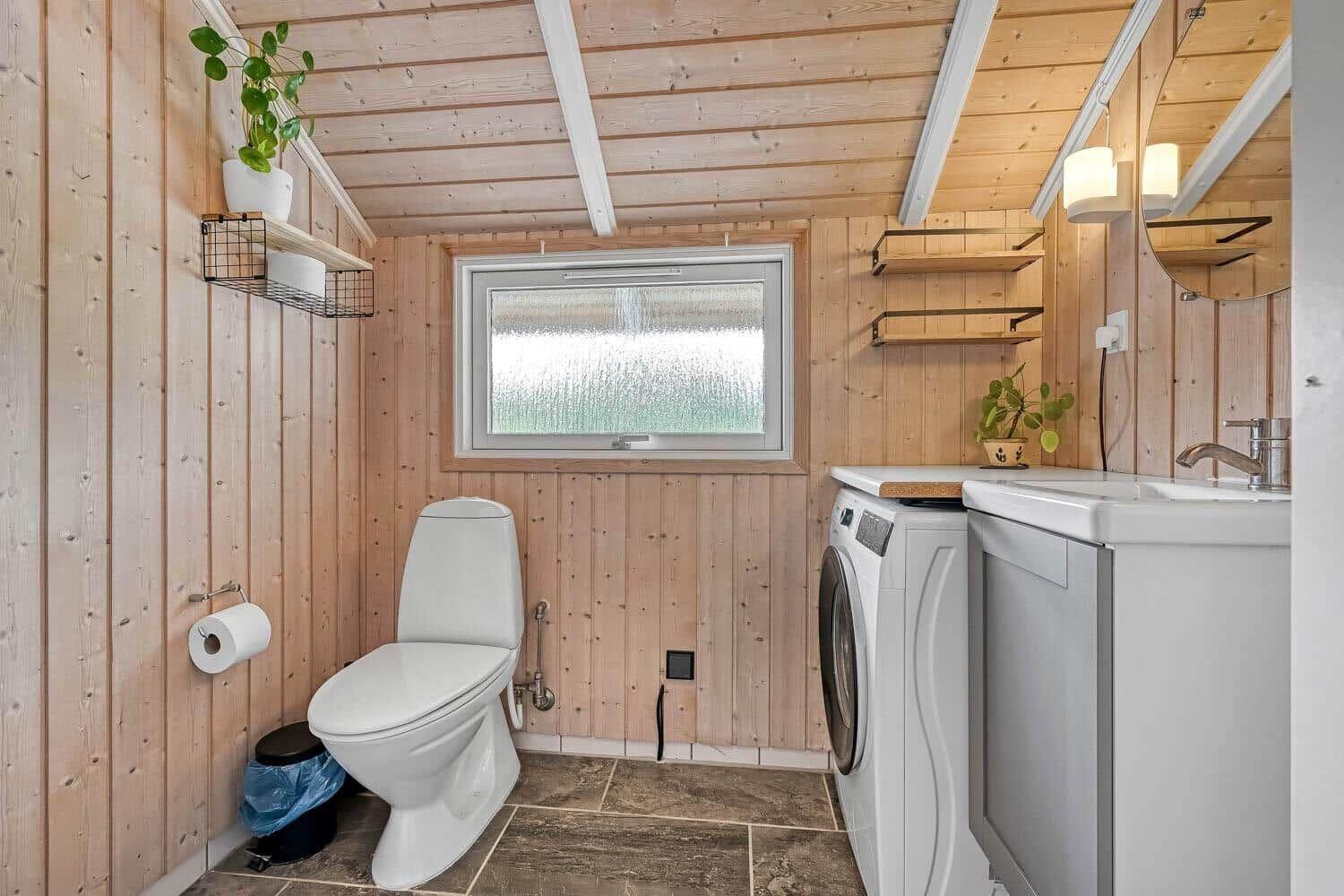 Bad mit Toilette, Waschmaschine und Waschbecken. Holzwände und gefliestes Boden.