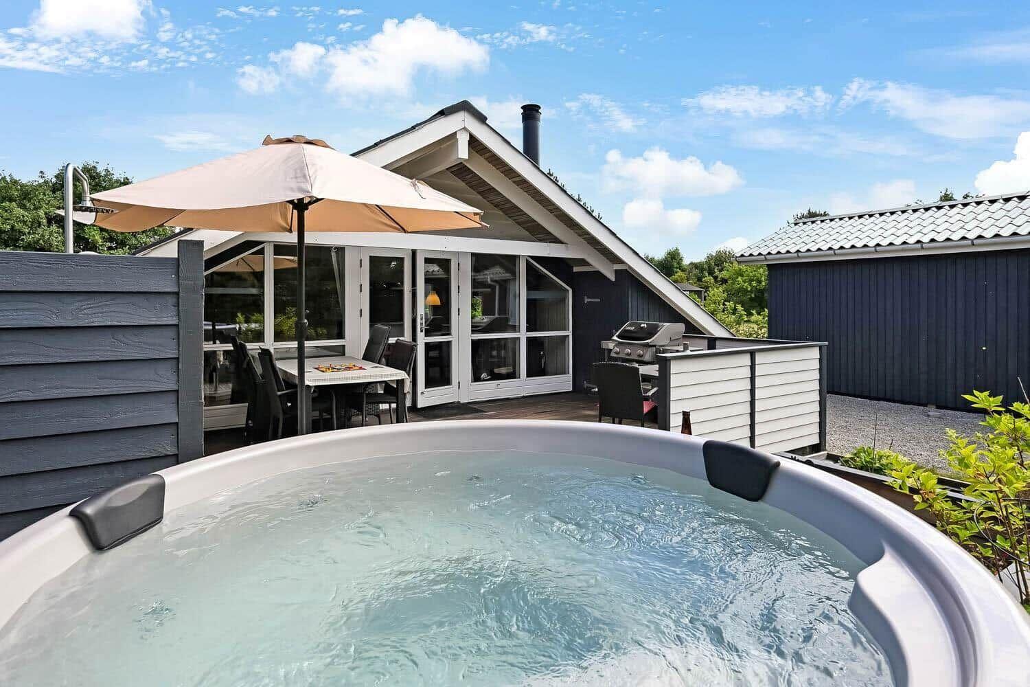 Hütte mit Whirlpool, Grill und Terrasse unter blauem Himmel.