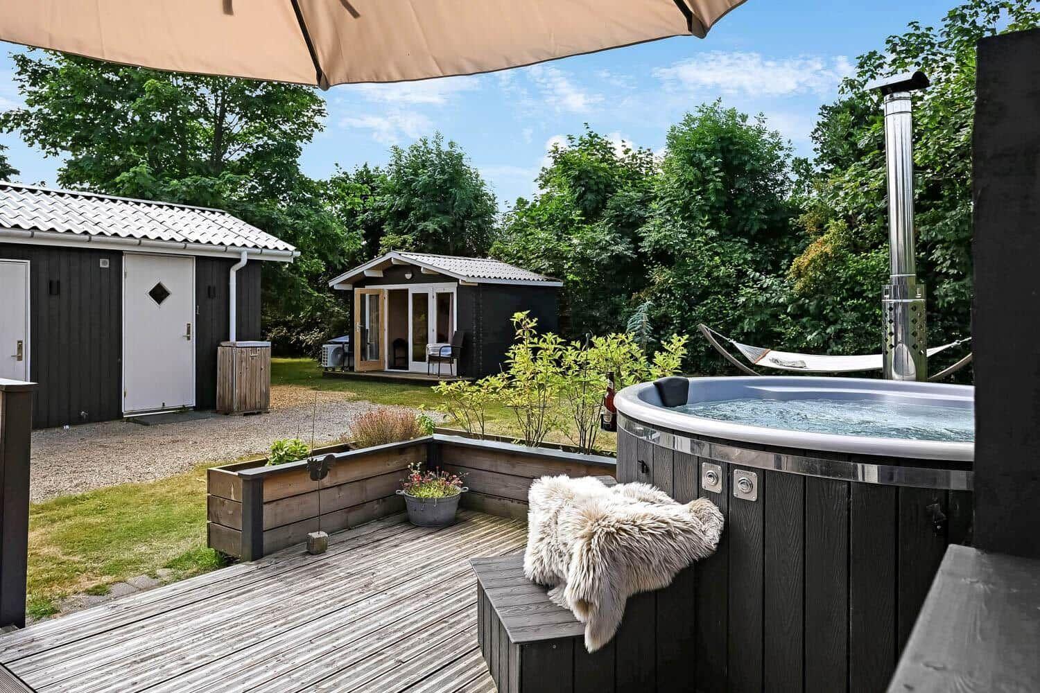 Hochwertiger Whirlpool auf Terrasse mit Blick auf Garten und Hütten.