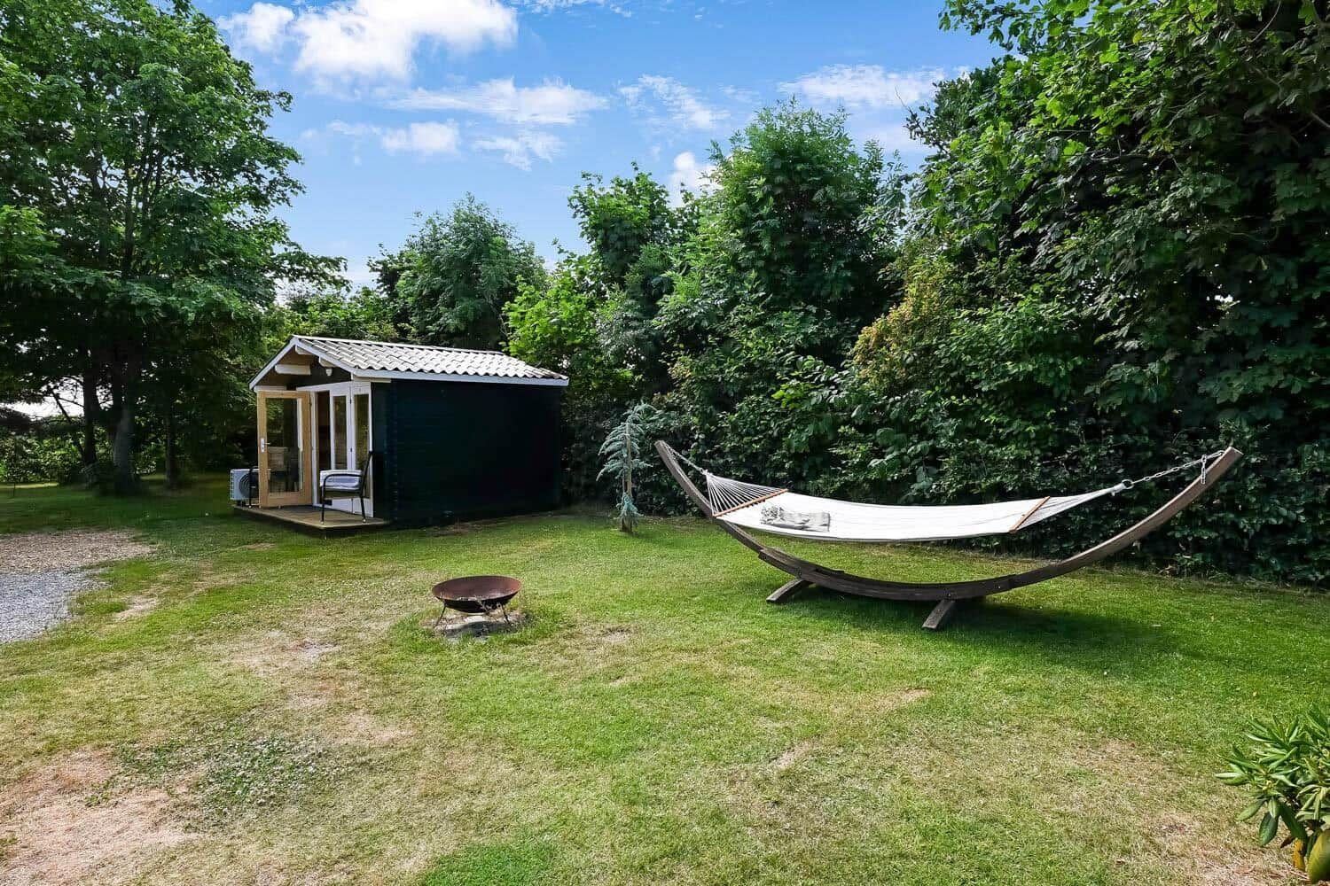 Hängemattensitzplatz vor einem Gartenhaus mit Grill und grünem Rasen.