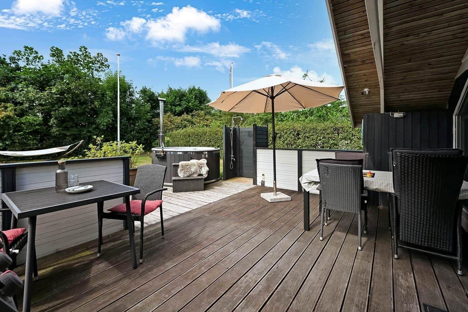 Terrasse mit Tisch, Stühlen, Sonnenschirm und Whirlpool. Hintergrund mit Bäumen und blauem Himmel.