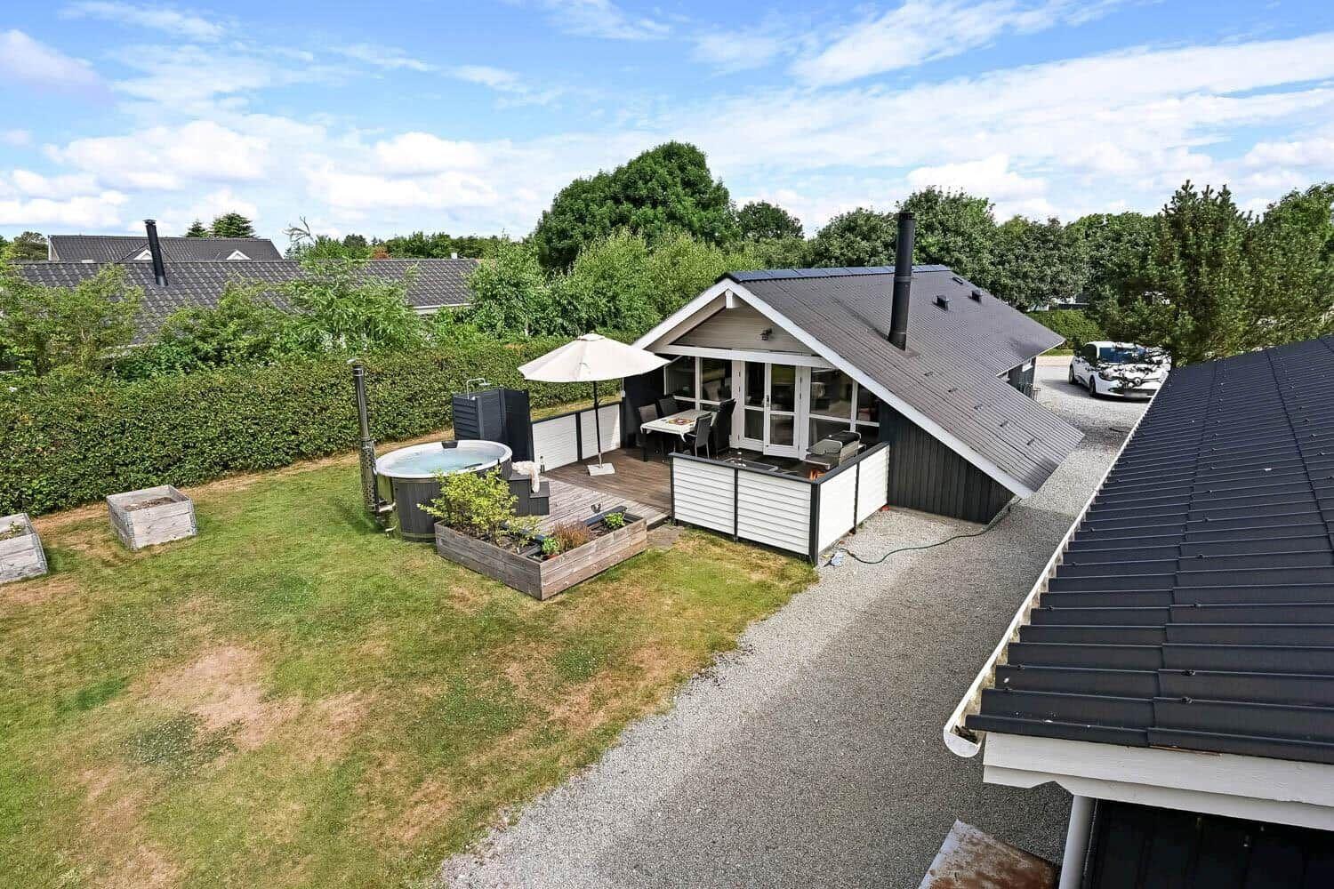 Haus mit Garten, Whirlpool und Terrasse unter blauem Himmel.