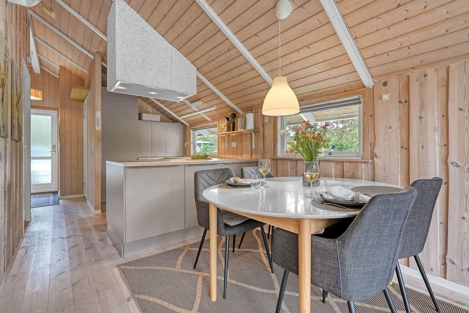 Küche und Essbereich mit Holzwand und -decke. Runder Tisch mit Stühlen und Fenster.