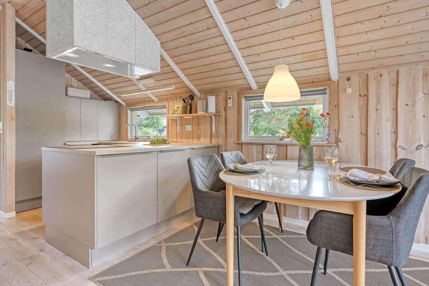 Küche und Essbereich mit Holzwand und -decke, runden Tisch und grauen Stühlen.