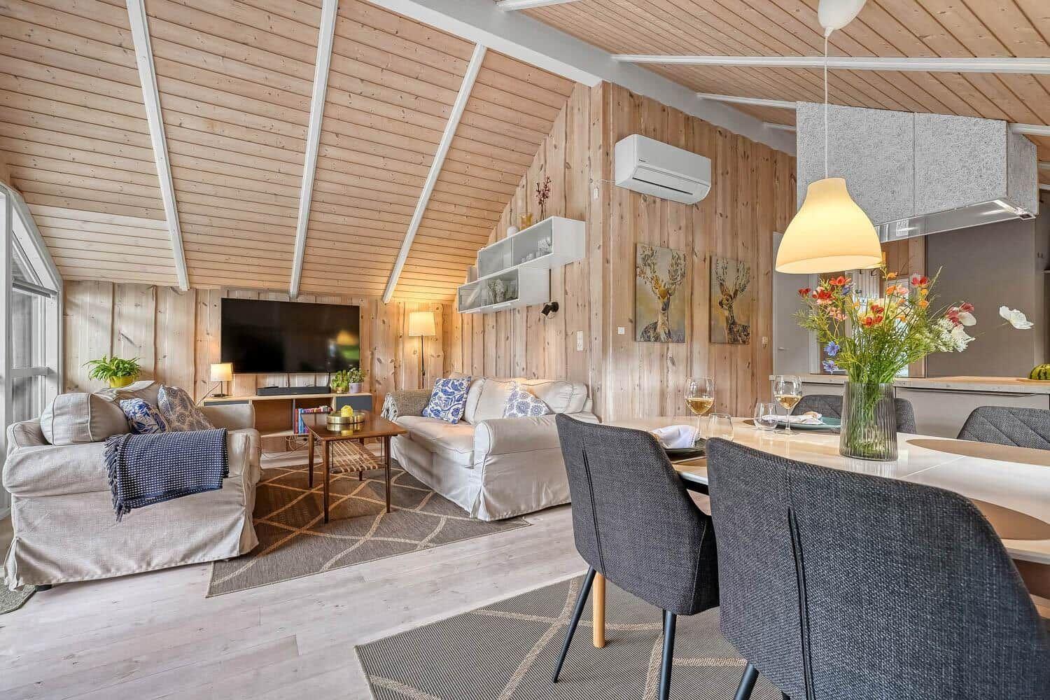 Wohn- und Essbereich mit Holzwand, Sofa, Fernseher und Esstisch mit Stühlen.