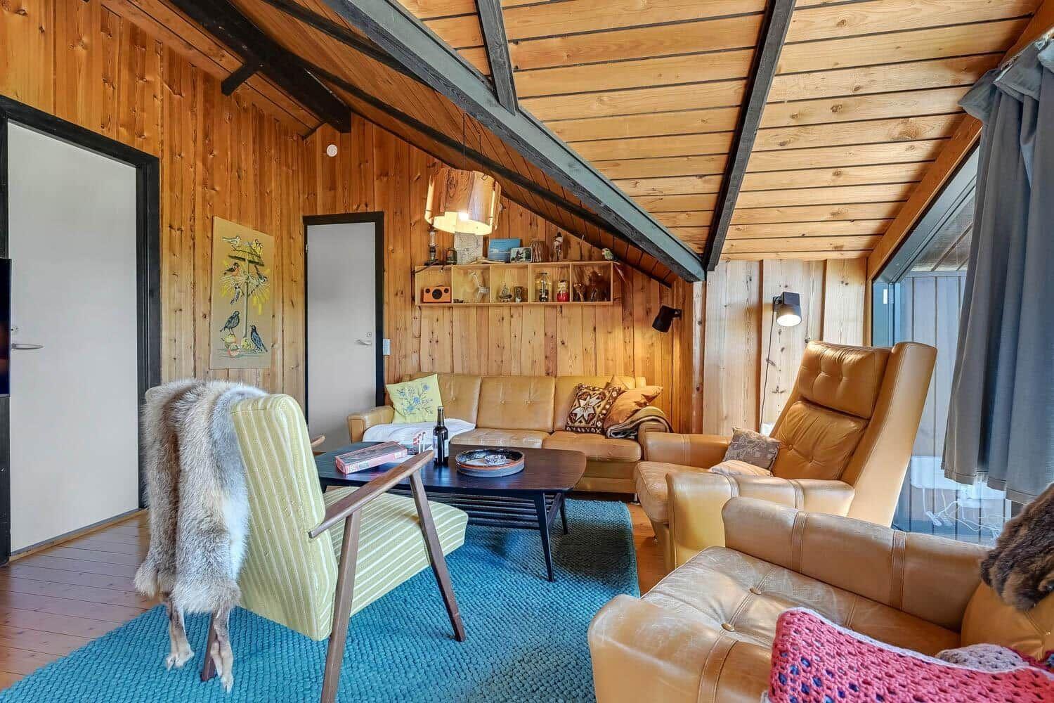Wohnraum mit Holzwänden, Sofa, Sessel und blauem Teppich unter Holzdach.