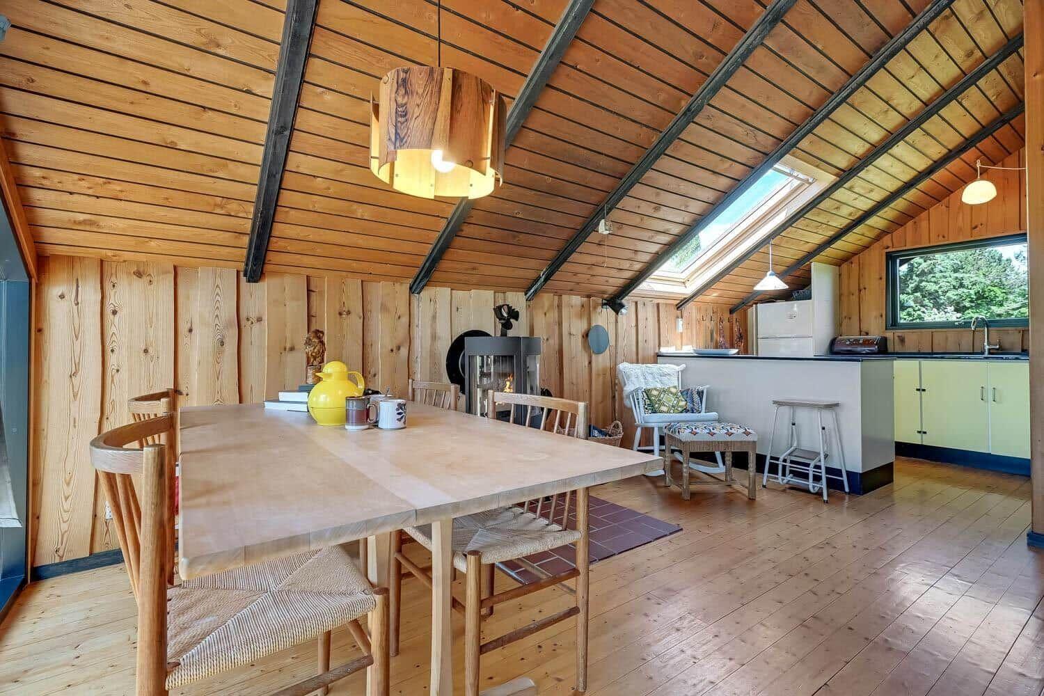 Holzgetäfelte Küche mit Esstisch, Kamin und Fenster. Holzdecke mit Balken.