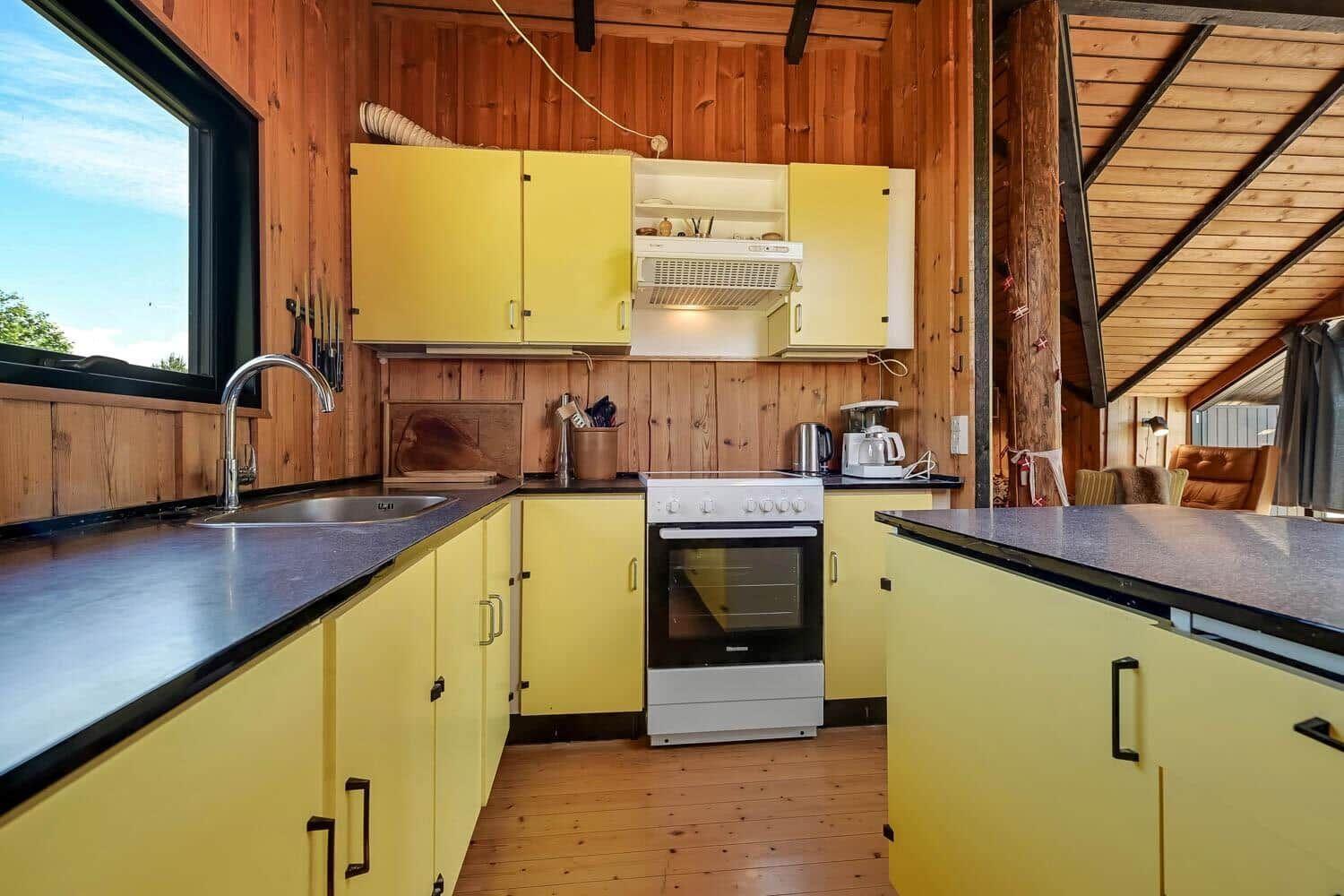Küche mit gelben Schränken, Edelstahlspüle und Holzwandverkleidung.