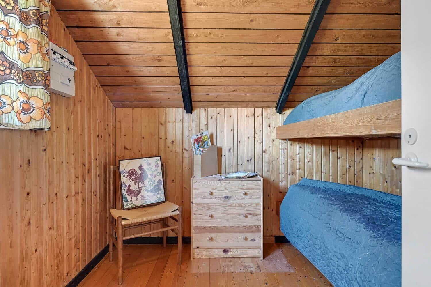 Ein Schlafzimmer mit Holzwand, Doppelbett und Schrank. Ein Stuhl mit Bild steht daneben.