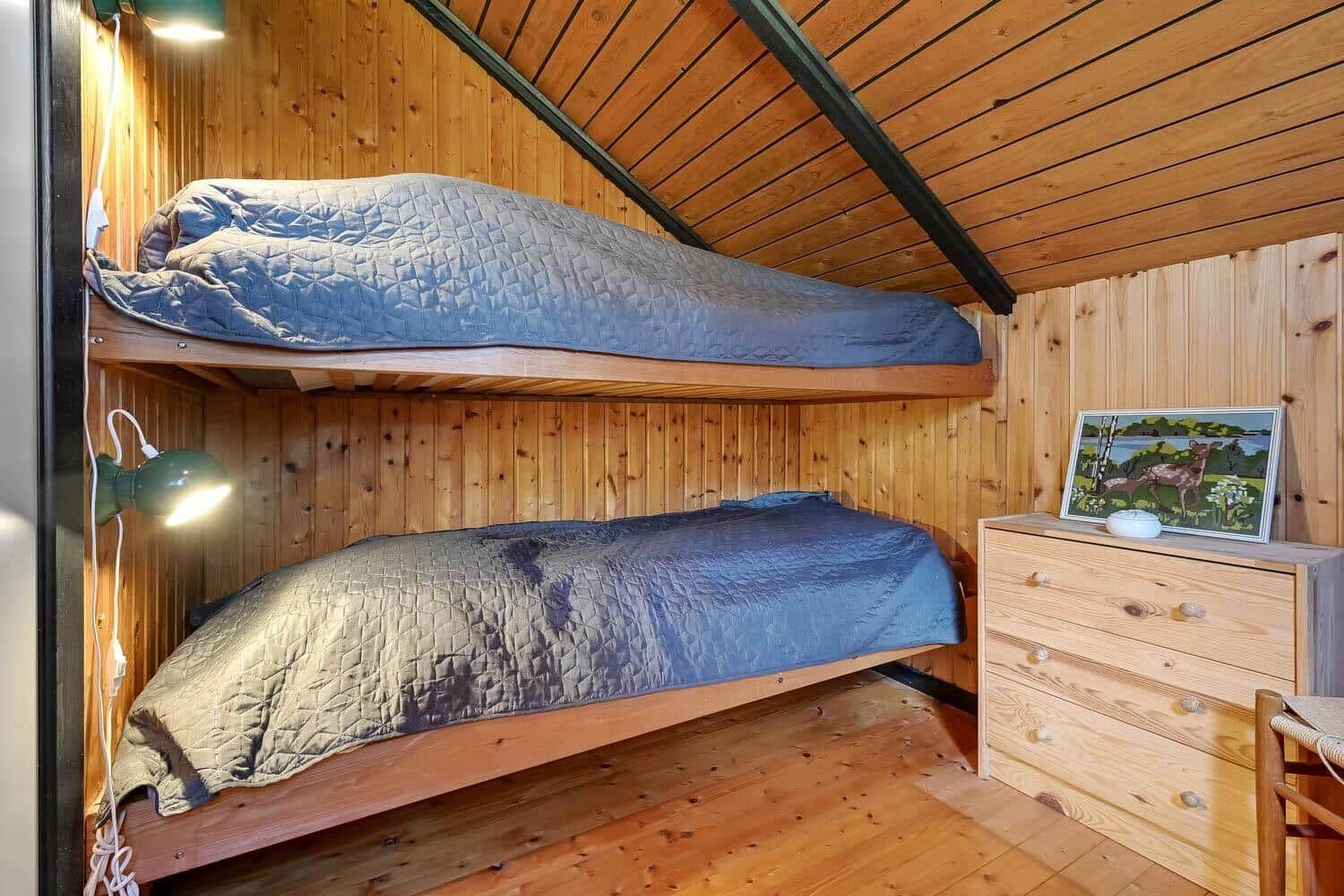 Zimmer mit zwei Etagenbetten, Holzwand und -decke, Schrank und Wandbild.