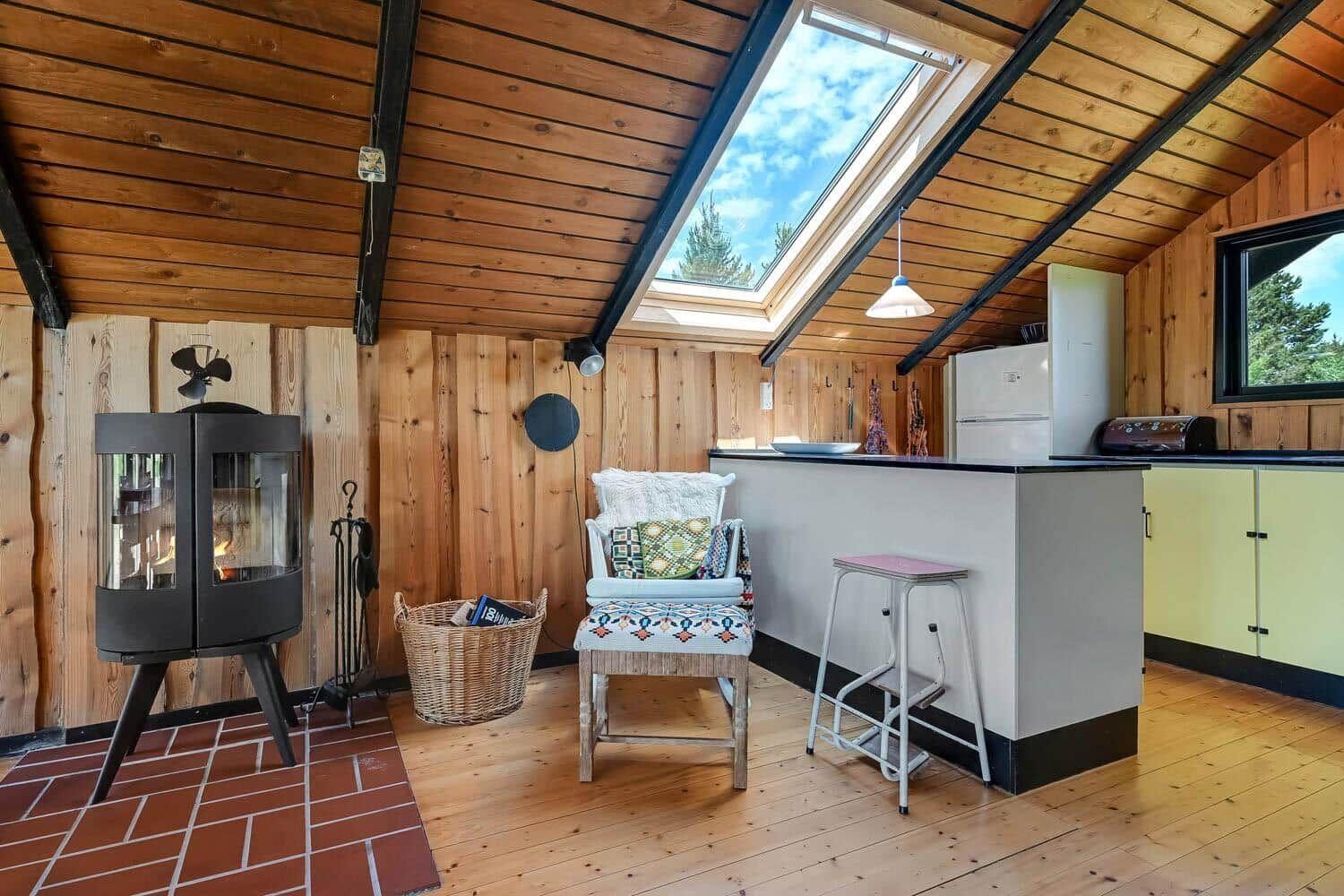 Wohnbereich mit Kamin, Sitzgelegenheit und Küchenbereich unter Holzdecke mit Dachfenster.