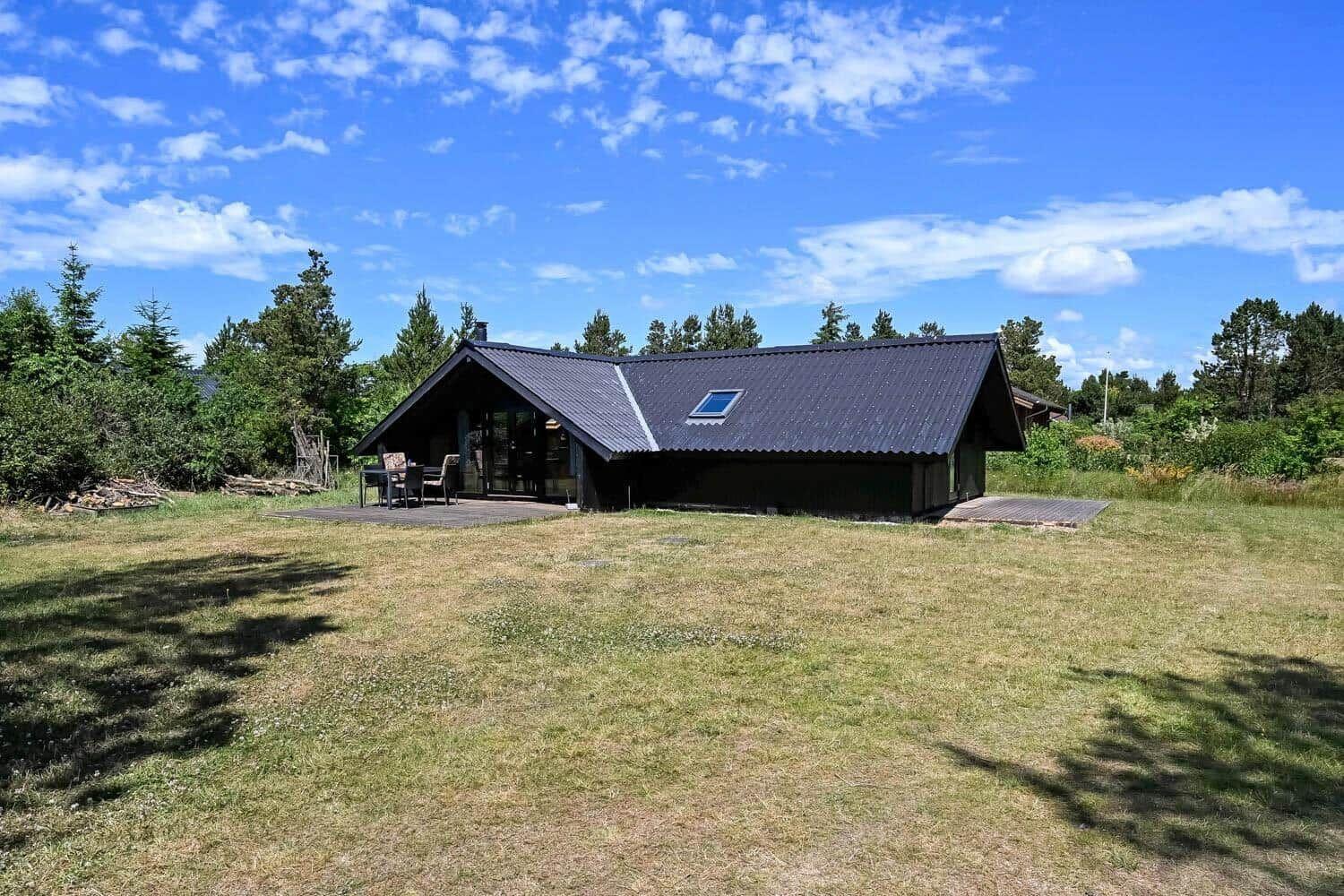 Holzhütte mit Terrasse und Garten unter blauem Himmel.