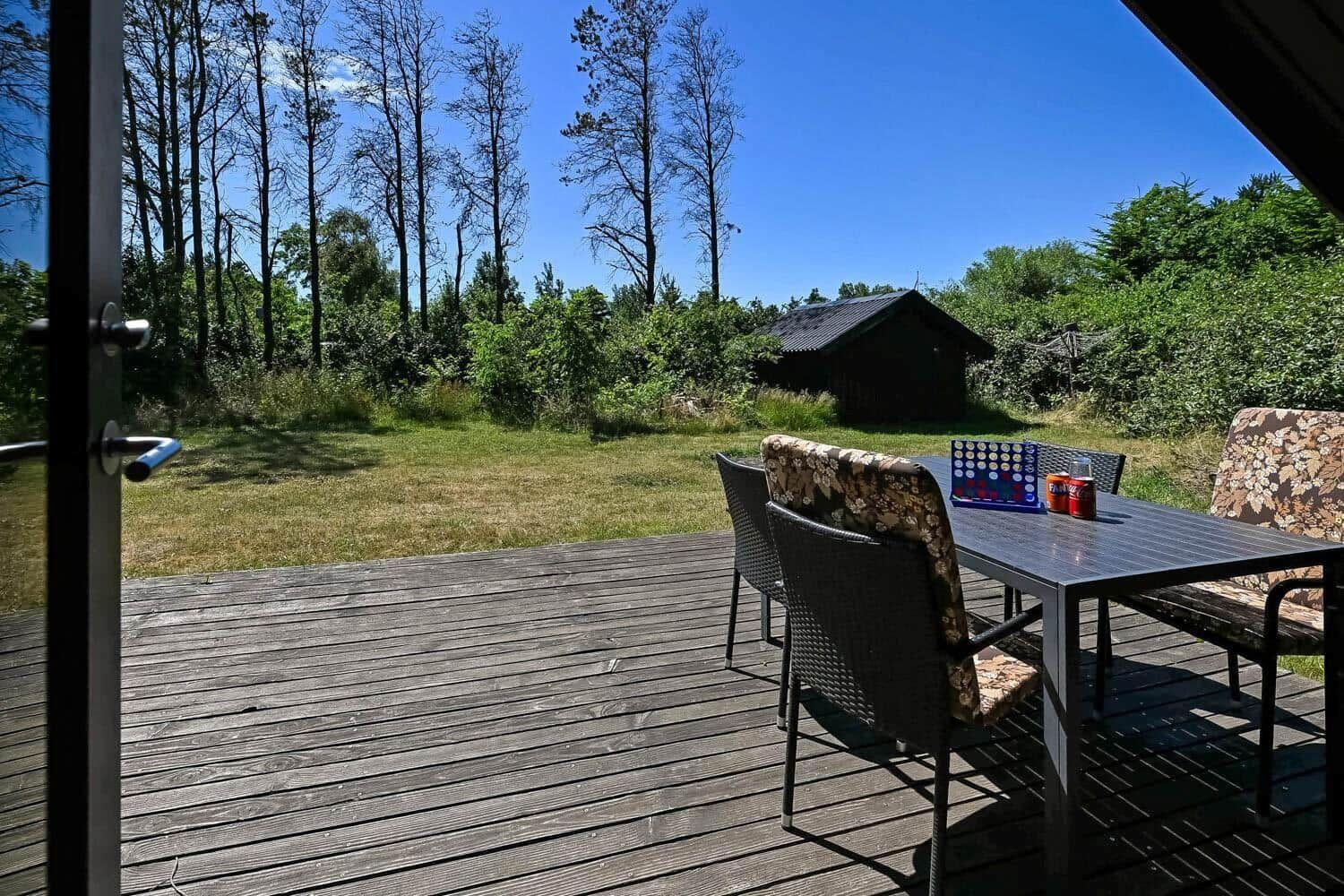 Terrasse mit Tisch und Stühlen, Blick auf Grasfläche und Wald.