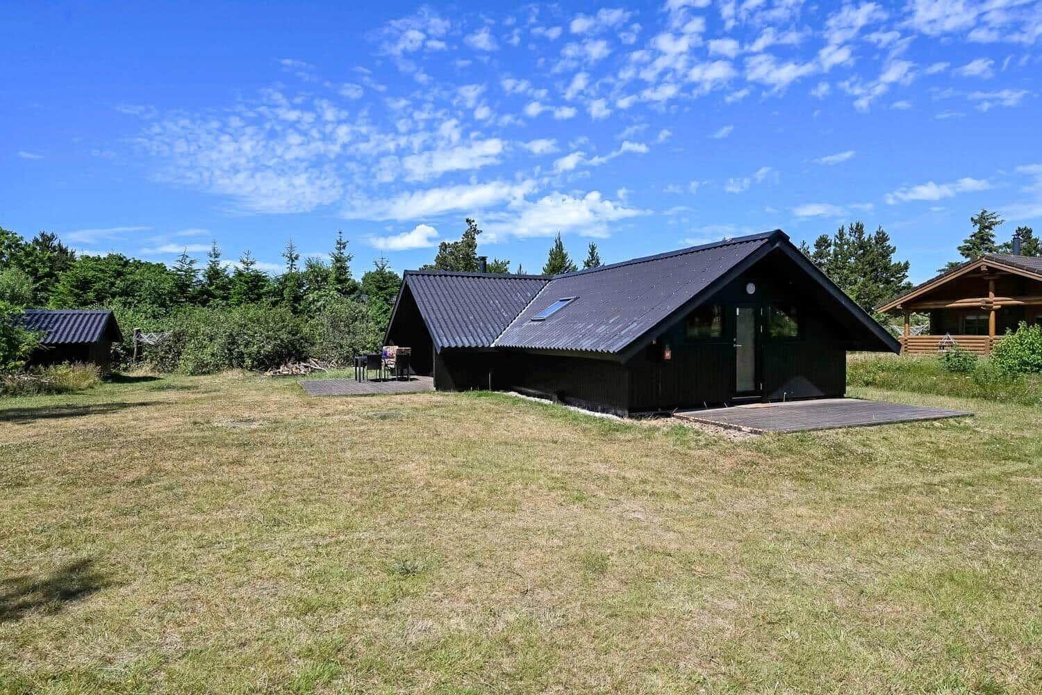 Schwarze Holzhütte mit Dachterrasse und Grillplatz auf grünem Grundstück