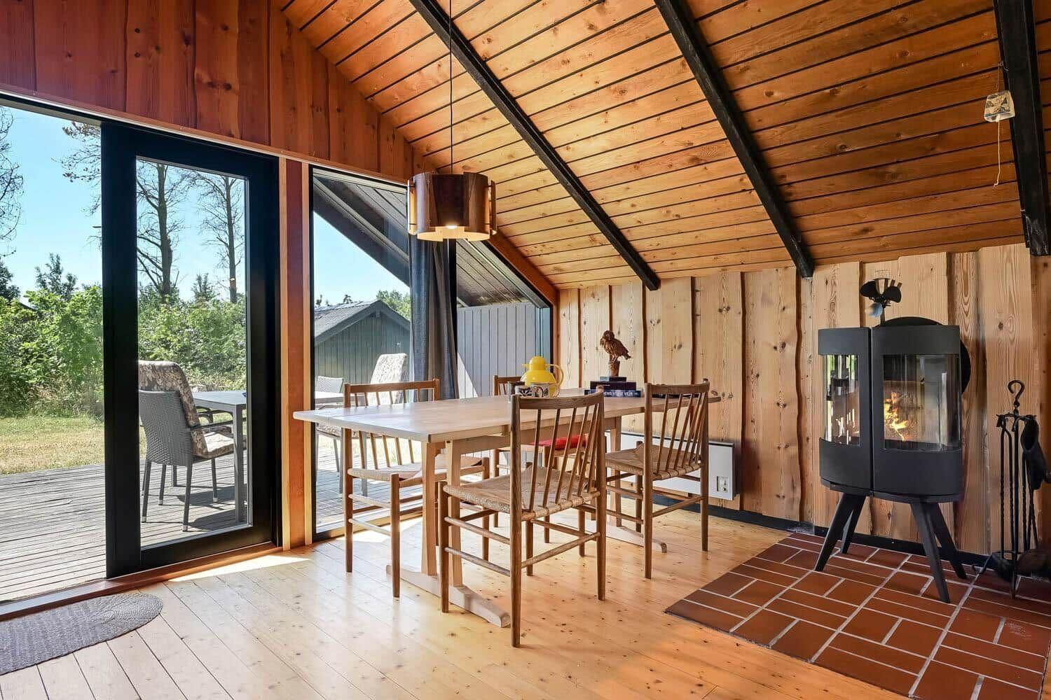 Esszimmer mit Holztisch, Stühlen und Kaminofen. Große Glasfront mit Blick auf Terrasse.