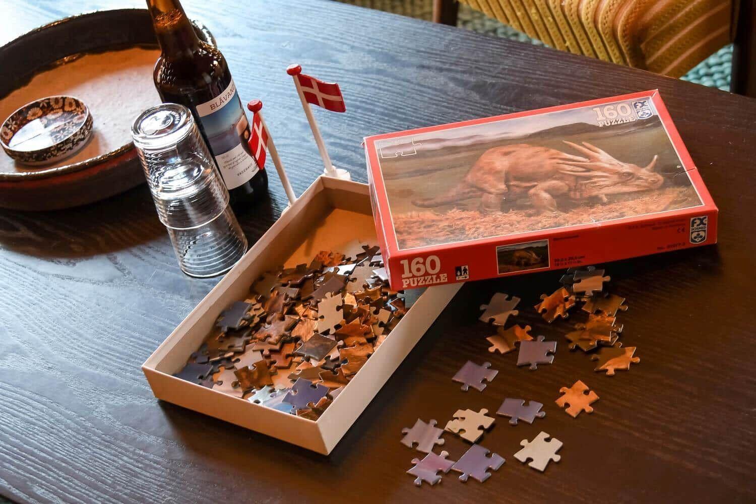 Ein Puzzle mit 160 Teilen liegt auf einem Tisch, daneben eine Flasche und kleine Flaggen.