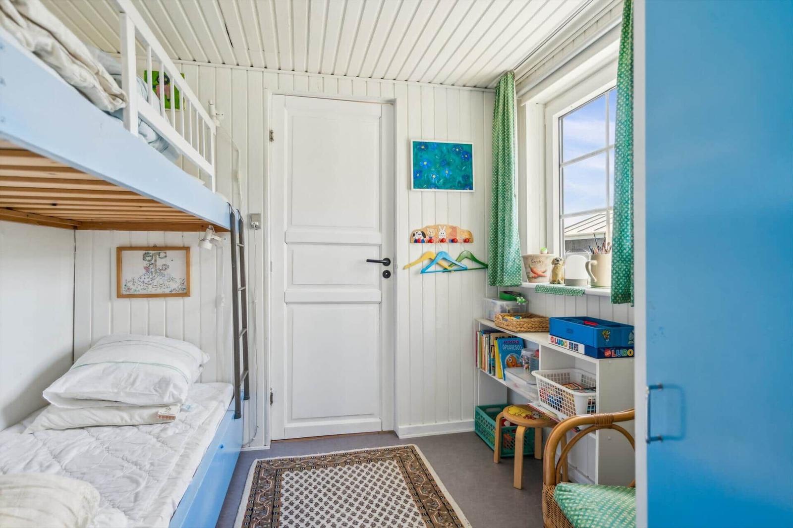 Ein Schlafzimmer mit einem Doppelstockbett, einem Schreibtisch und einem Fenster mit grünen Vorhängen.