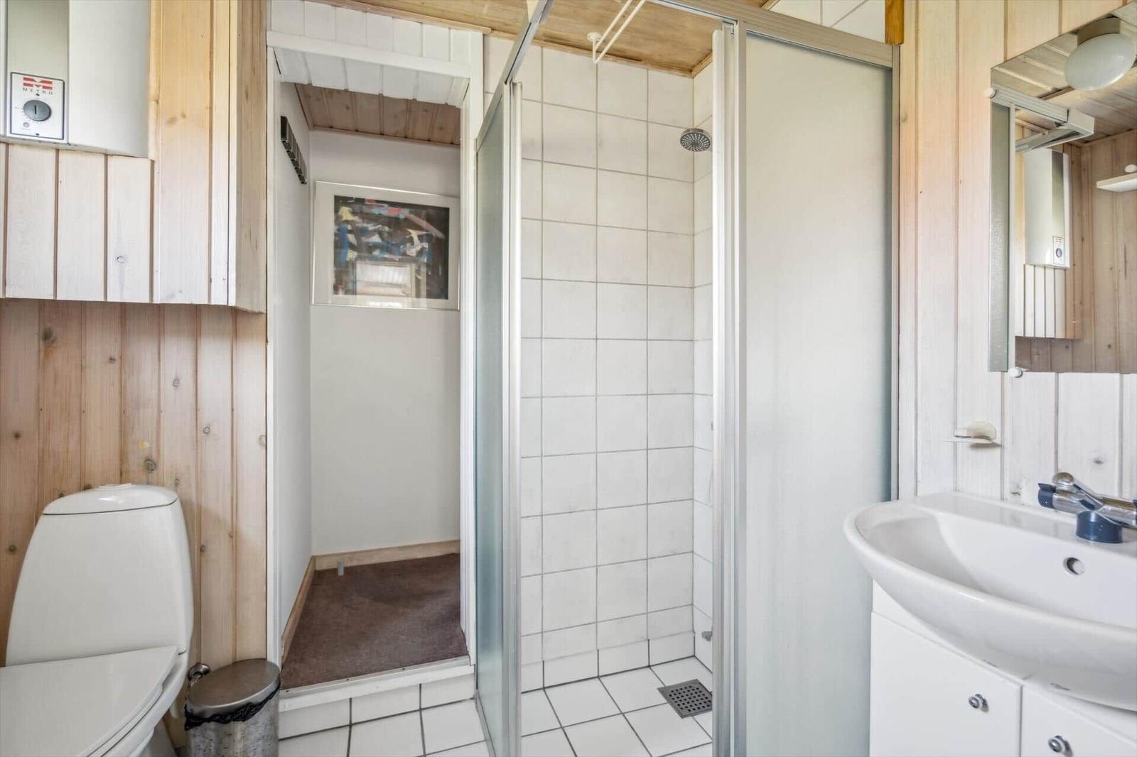 Badezimmer mit Dusche, Waschbecken und Toilette. Holzwände und Fliesenboden.