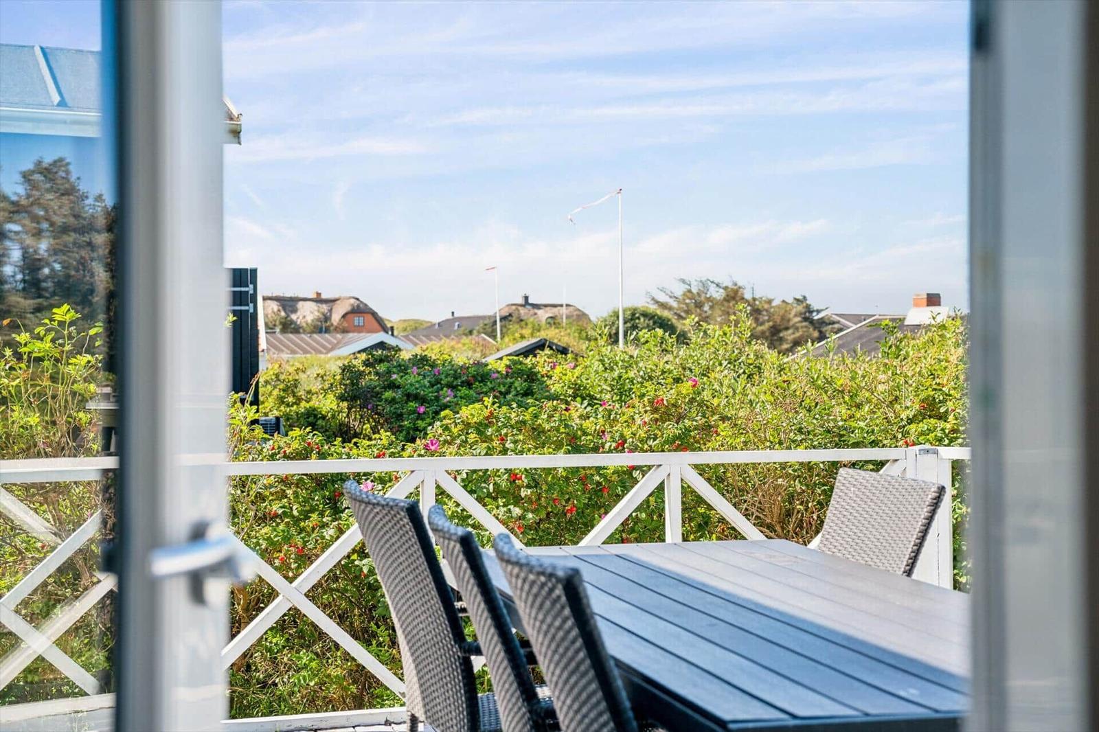 Terrasse mit Tisch und Stühlen. Blick auf grüne Hecke und Häuser im Hintergrund.