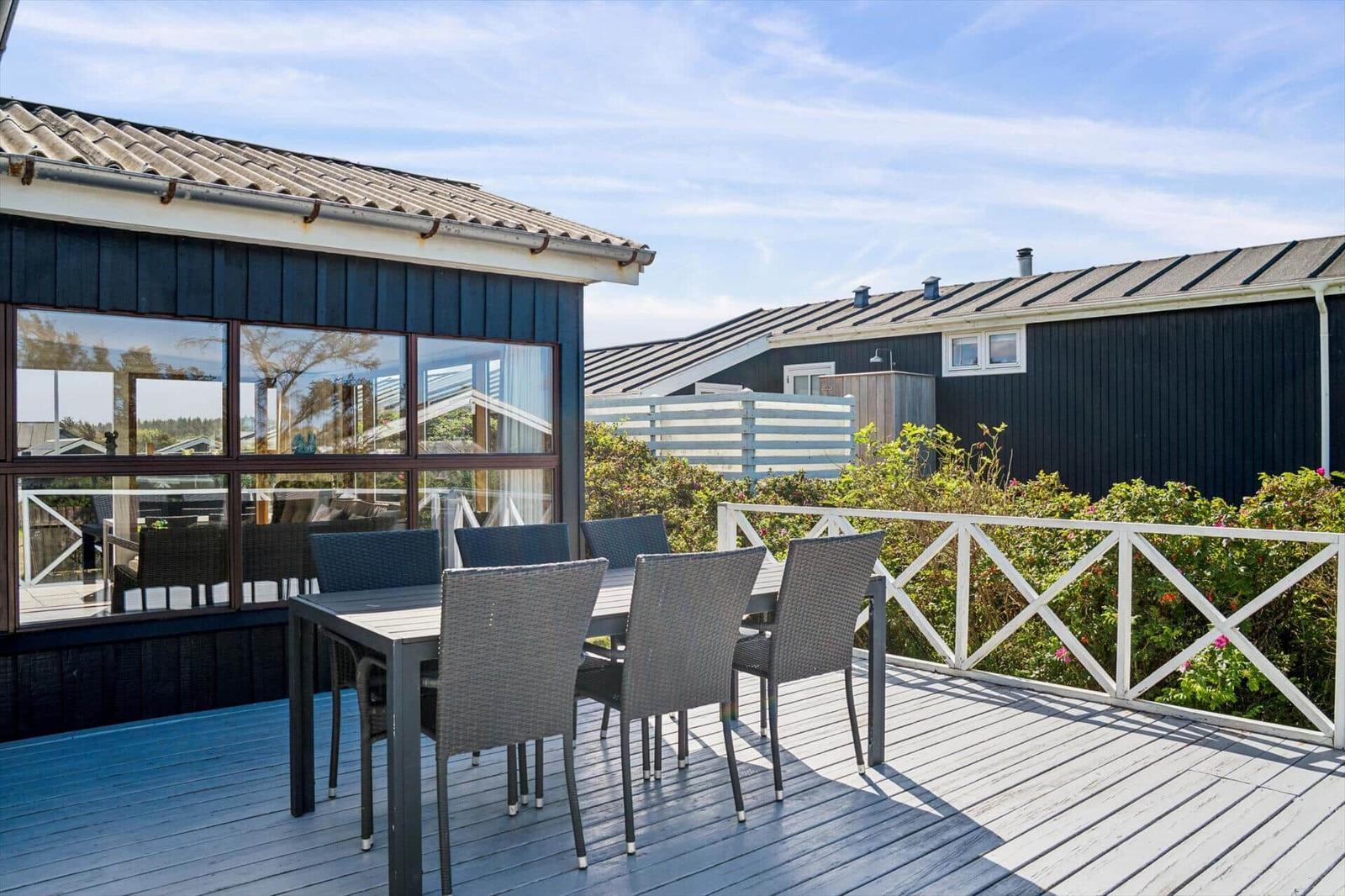 Terrasse mit Tisch und Stühlen, Blick auf schwarze Häuser und grüne Hecke.
