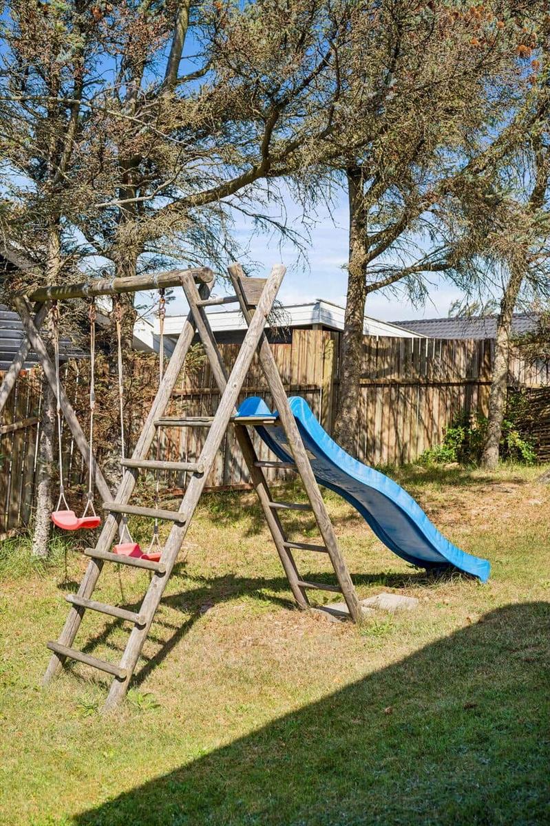 Hinterhof mit Holzspielgeräten, Rutsche und Schaukel unter Bäumen.