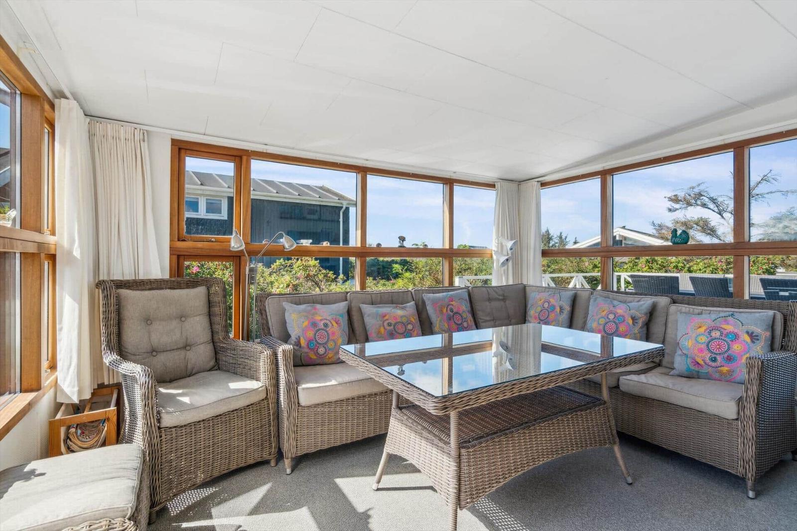Glashalle mit Sitzgruppe, Tisch und Blick auf Garten.