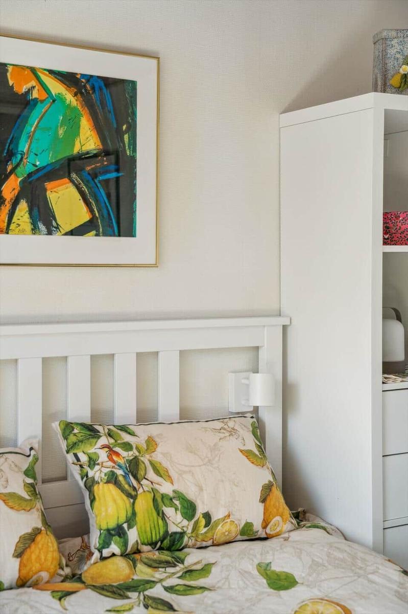 Schlafzimmer mit Bett, Kissen und Wandbild. Neben dem Bett steht ein weißer Schrank.